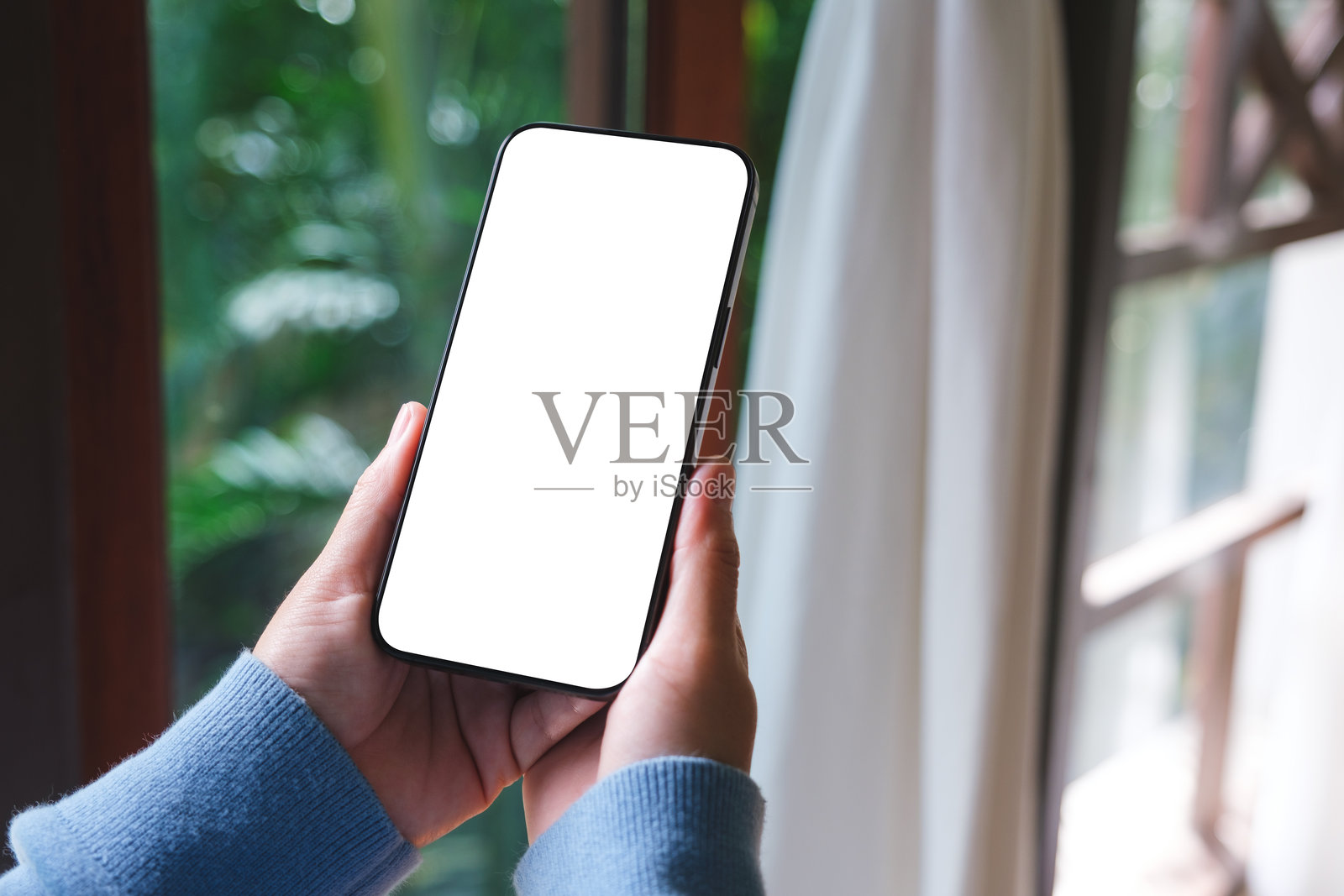 一名女子在家中手持手机，屏幕为空白的样机图照片摄影图片