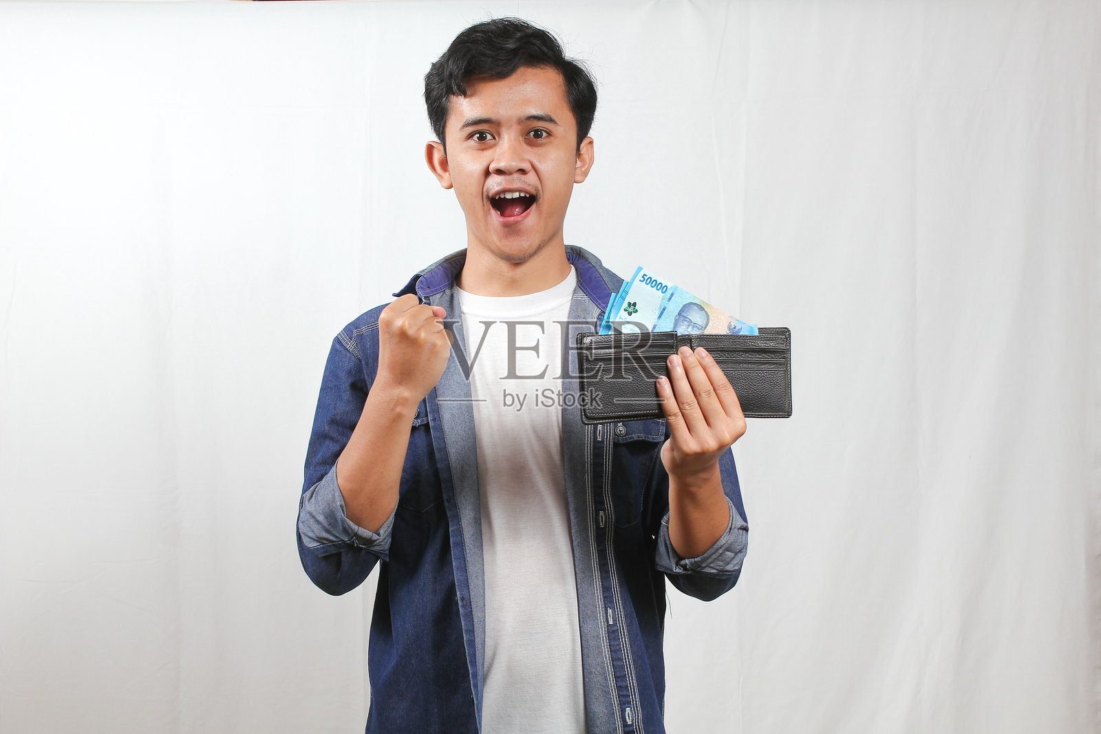 一名亚洲男子在白色背景下，手中拿着钱包里的钞票，庆祝成功。照片摄影图片