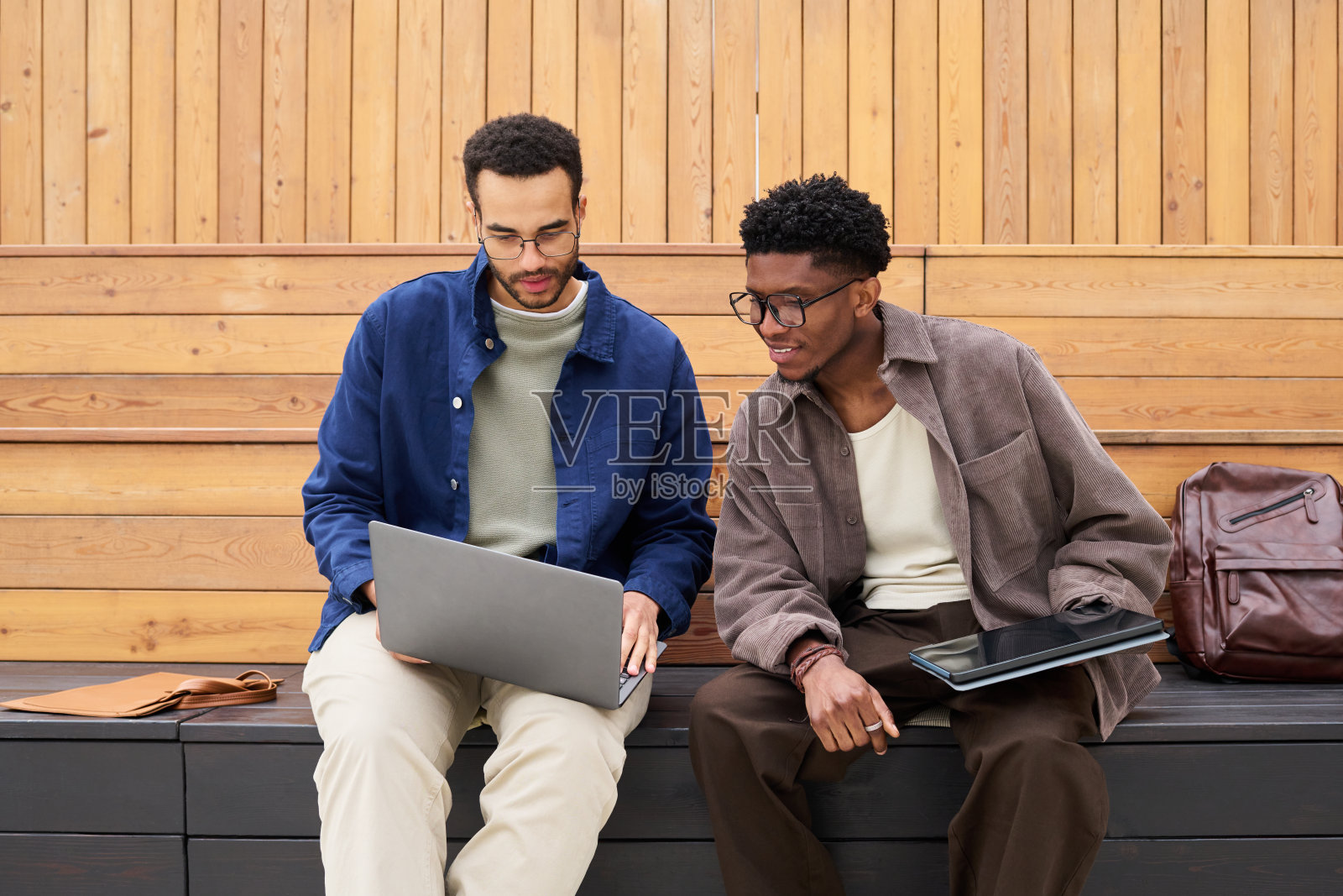 年轻男性在现代户外环境中协作，使用笔记本电脑和平板电脑照片摄影图片