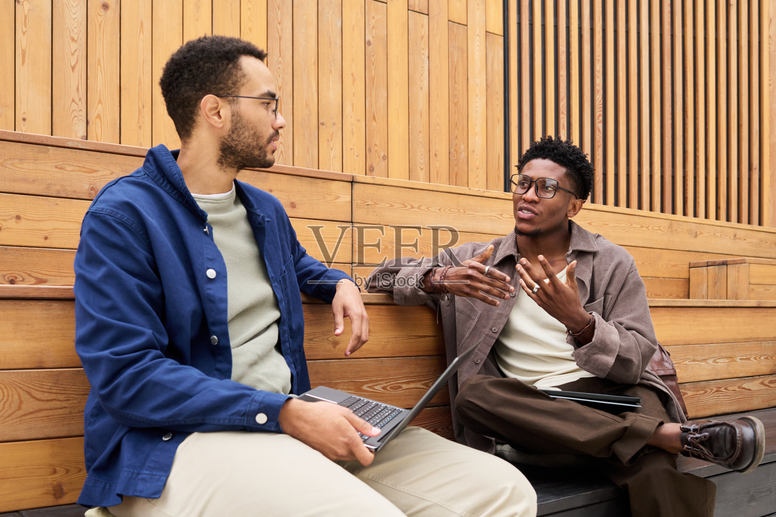 年轻的黑人男性在户外坐着，使用笔记本电脑讨论想法。照片摄影图片