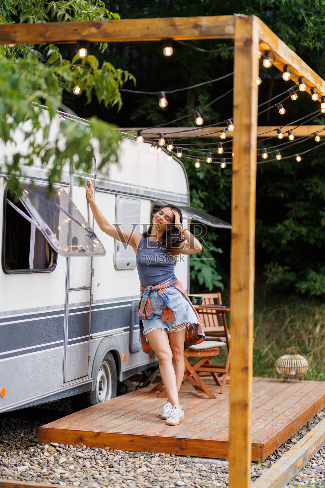 年轻漂亮的女人站在她的露营车入口处，在夜间停靠时微笑着。照片摄影图片