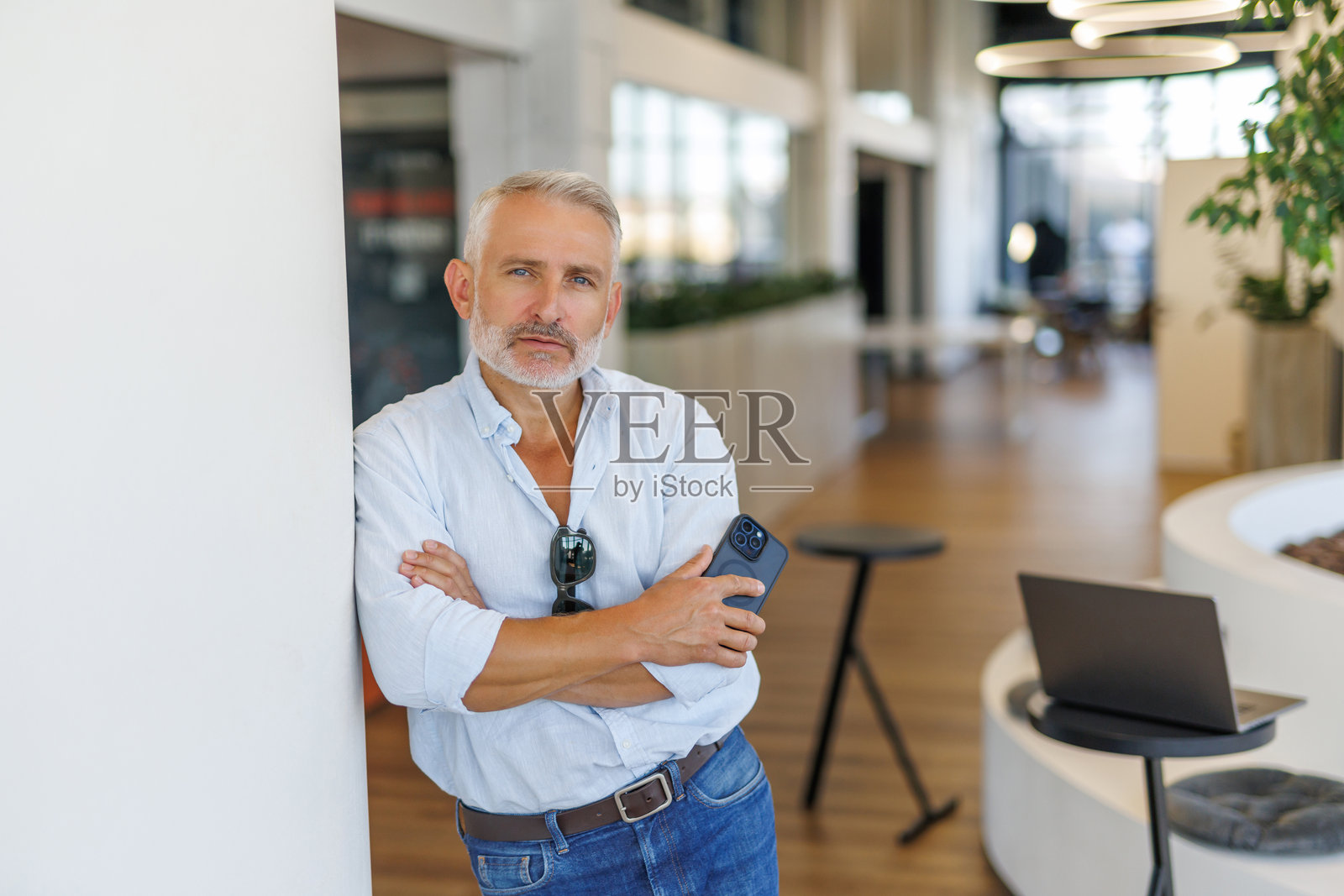 中年商人 executive 手持智能手机，面向镜头，站在办公室外。肖像。照片摄影图片