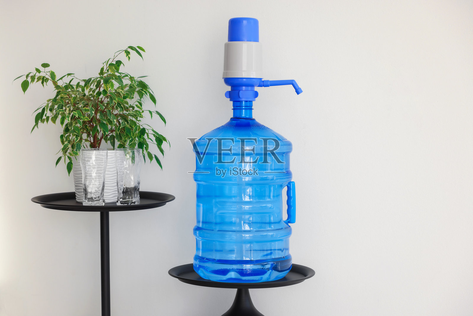 白色墙壁旁边的带水瓶、水泵、眼镜和室内植物的冷却器。留有文字空间照片摄影图片