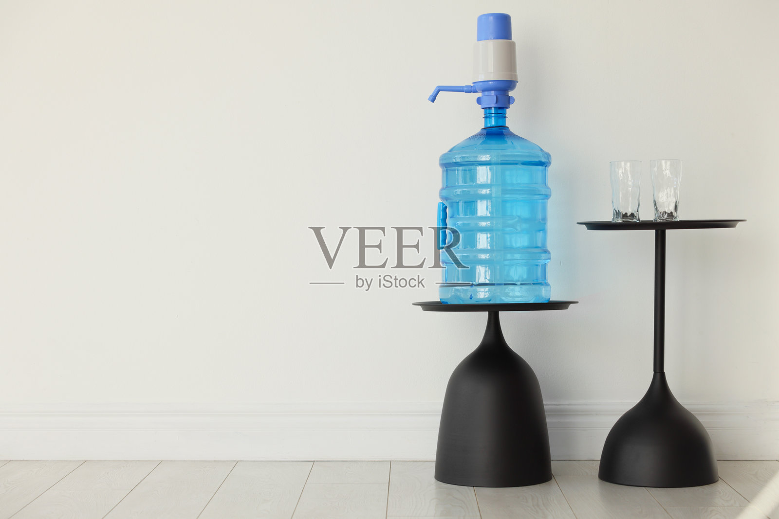 白色墙壁旁的带水、带泵和杯子的冷却瓶。留有文字空间照片摄影图片