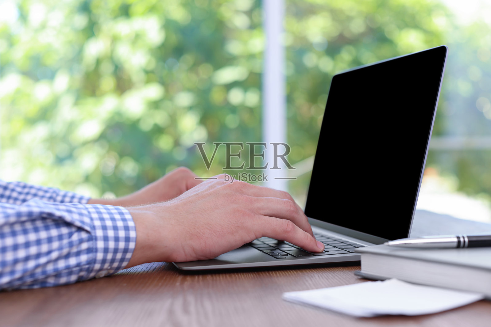 特写：男子在室内木桌上用笔记本电脑工作照片摄影图片