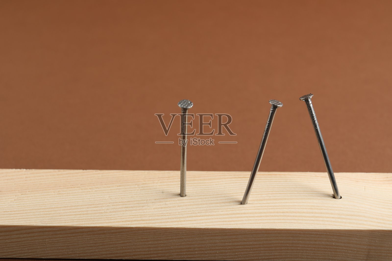特写镜头下木板上的金属钉，背景为棕色。留有文字空间。照片摄影图片