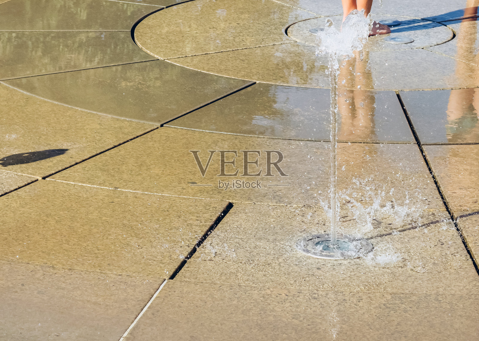 夏日炎炎，孩子们在喷泉中嬉戏，特写镜头捕捉到孩子们溅起水花的双脚，充满活力的户外活动与无忧无虑的假期乐趣。照片摄影图片