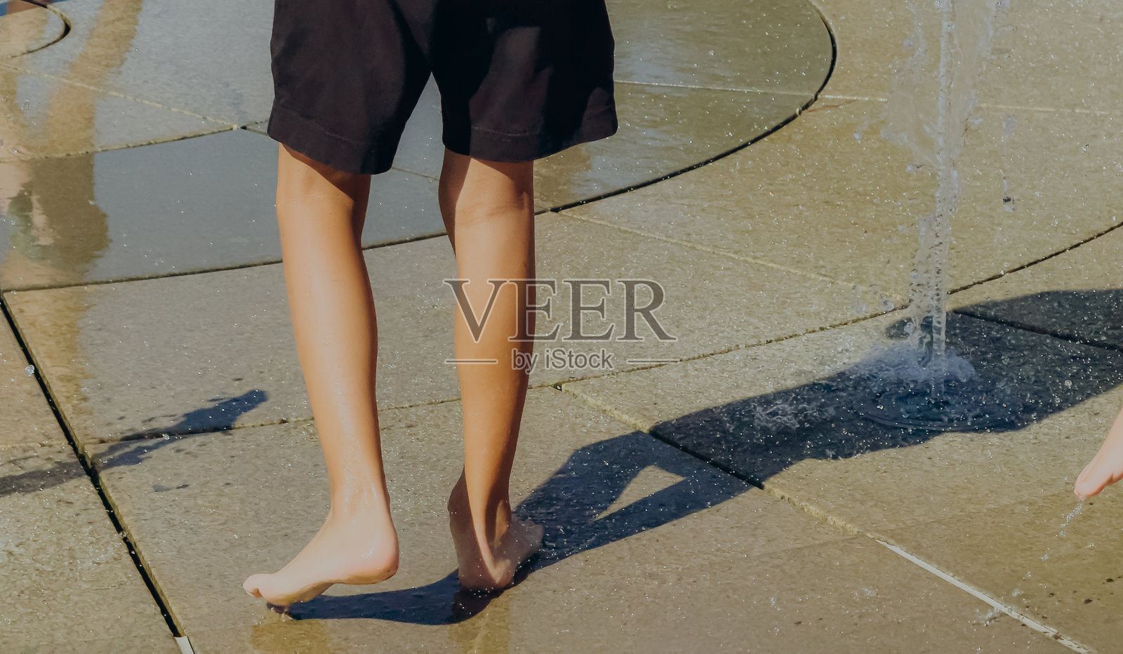 炎炎夏日，孩子们在喷泉里玩耍，特写镜头展示了孩子们溅起水花的脚，充满活力的户外活动和无忧无虑的假期乐趣。照片摄影图片