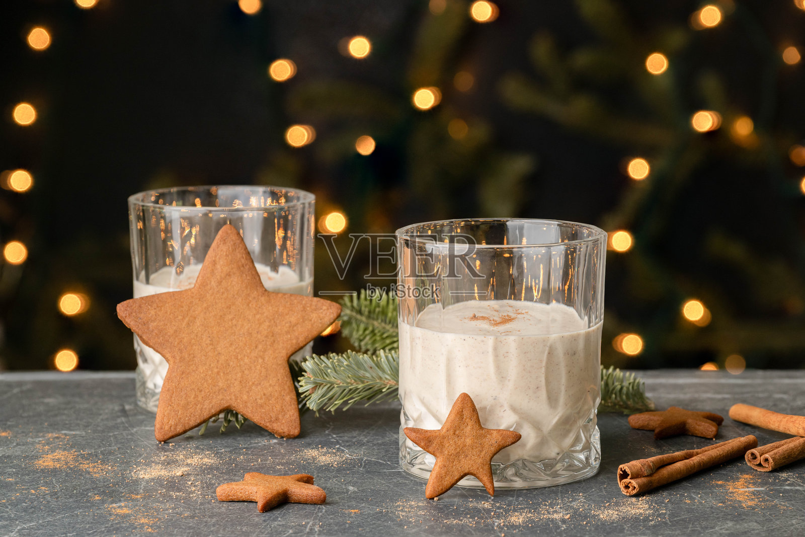 圣诞假日传统蛋酒放在大理石桌上，配有星形姜饼和肉桂棒，背景是点亮的圣诞树。照片摄影图片