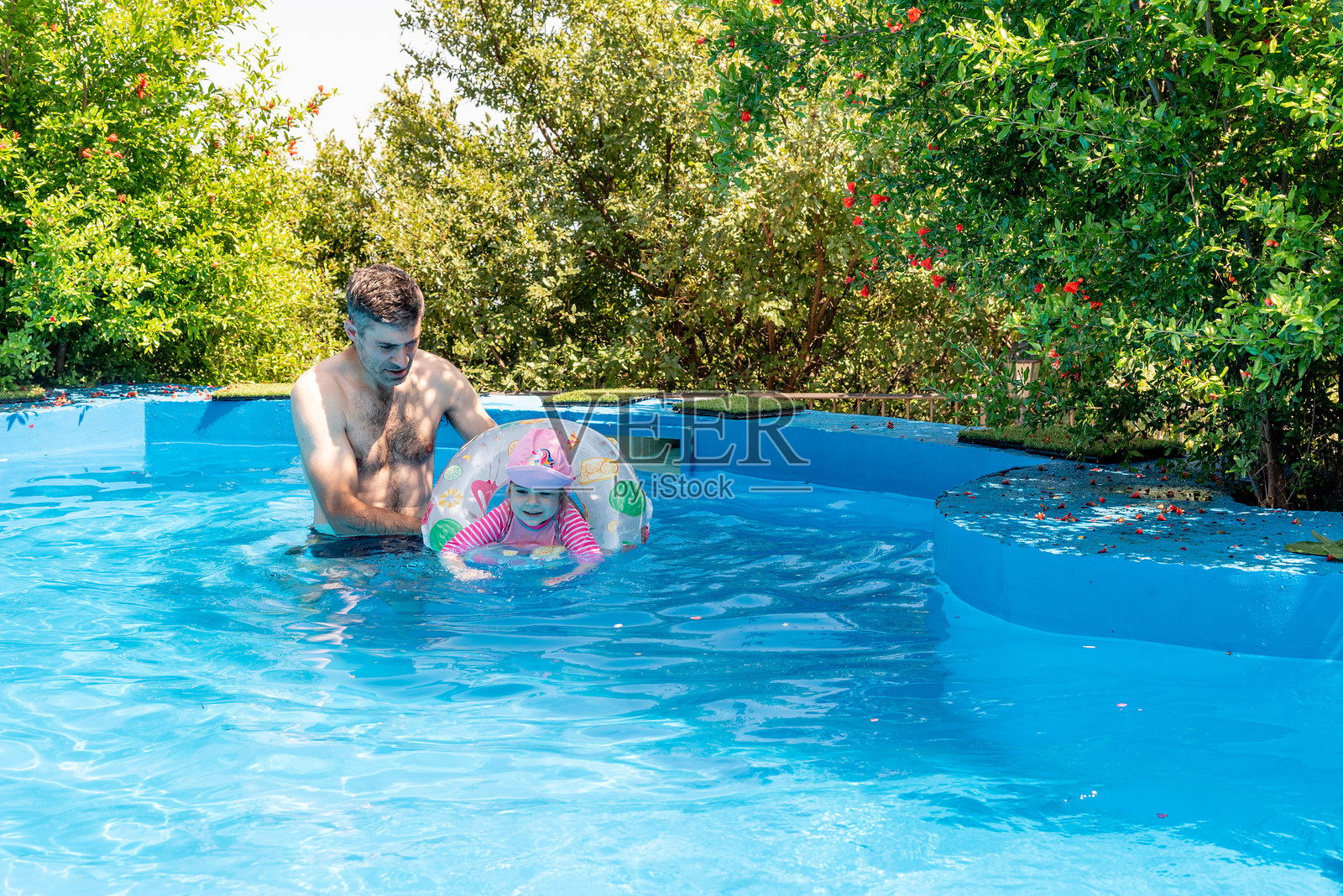 夏日晴天，爸爸和女儿在泳池里带着游泳圈游泳。照片摄影图片