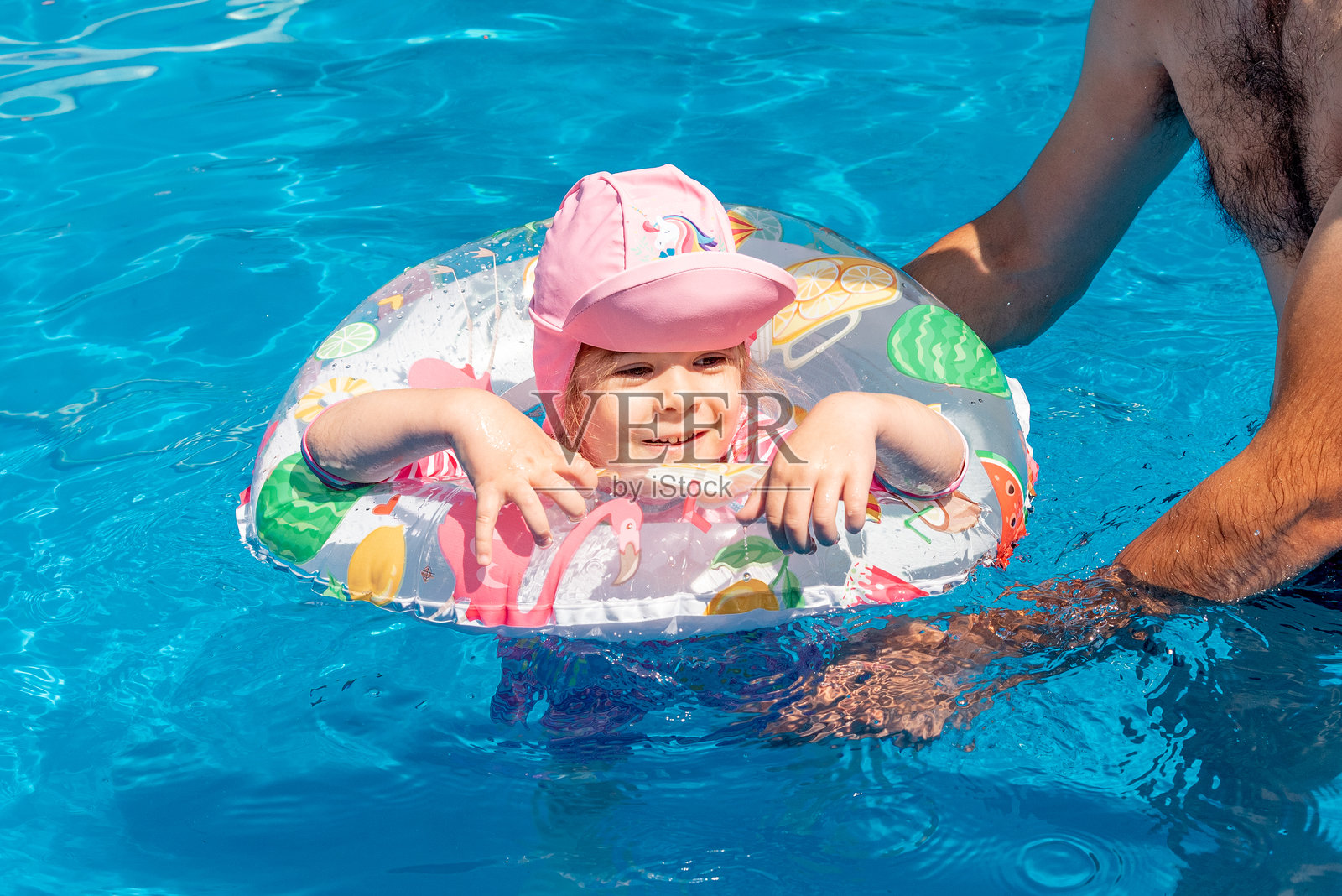 夏日晴天，爸爸和女儿在泳池里玩耍，旁边有一个充气泳圈。照片摄影图片