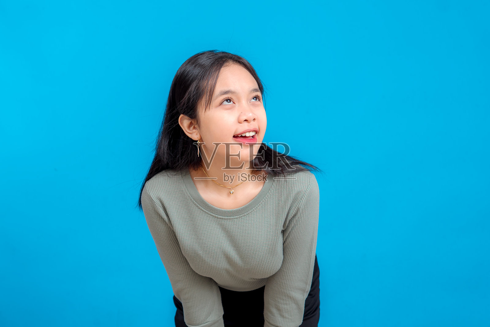 一位年轻亚洲女性，脸上带着好奇和灵感的表情，微微笑着向上看。背景为蓝色。象征着想象力、惊奇和乐观。照片摄影图片