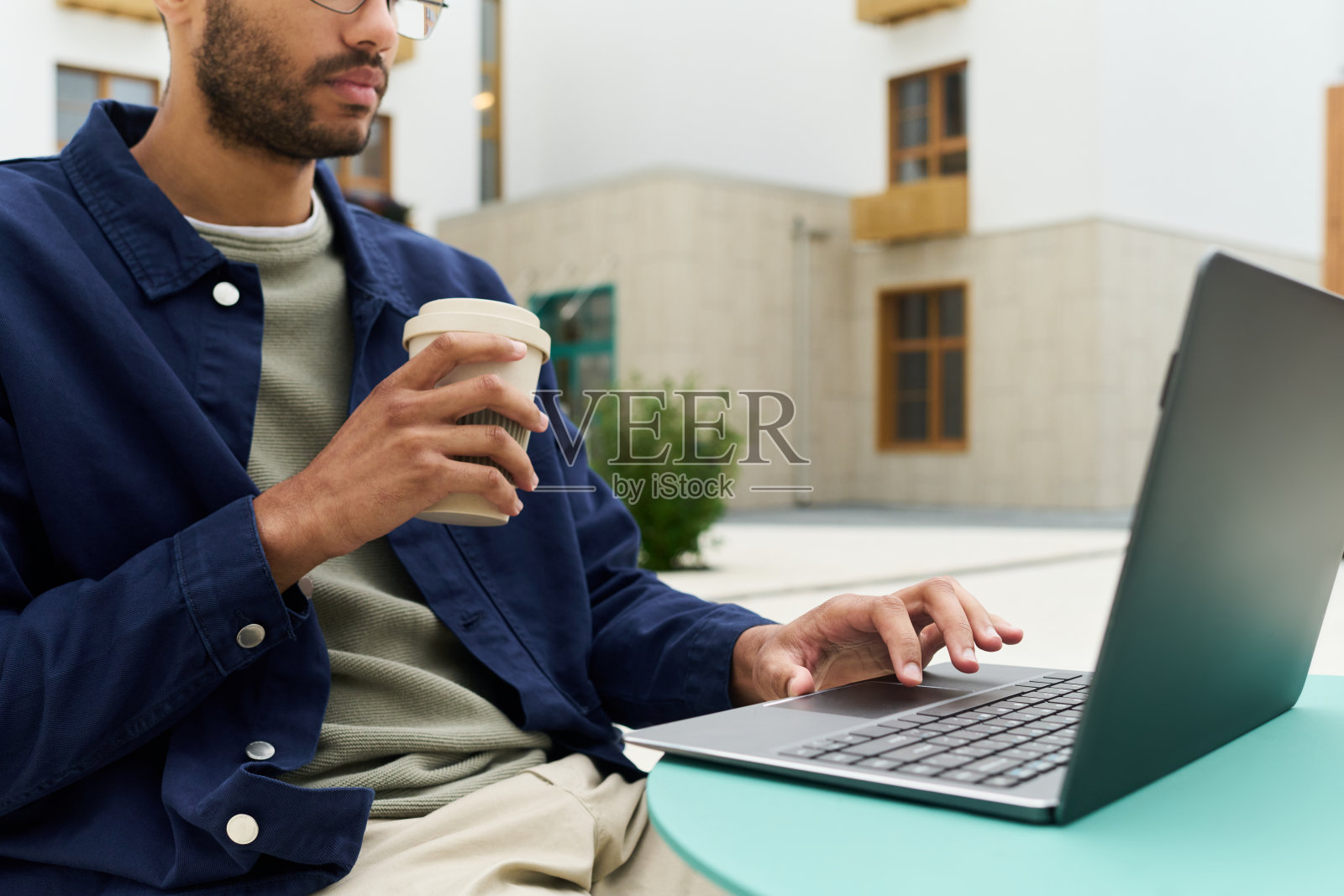 年轻的黑人男性一边用笔记本电脑远程工作，一边拿着咖啡杯照片摄影图片