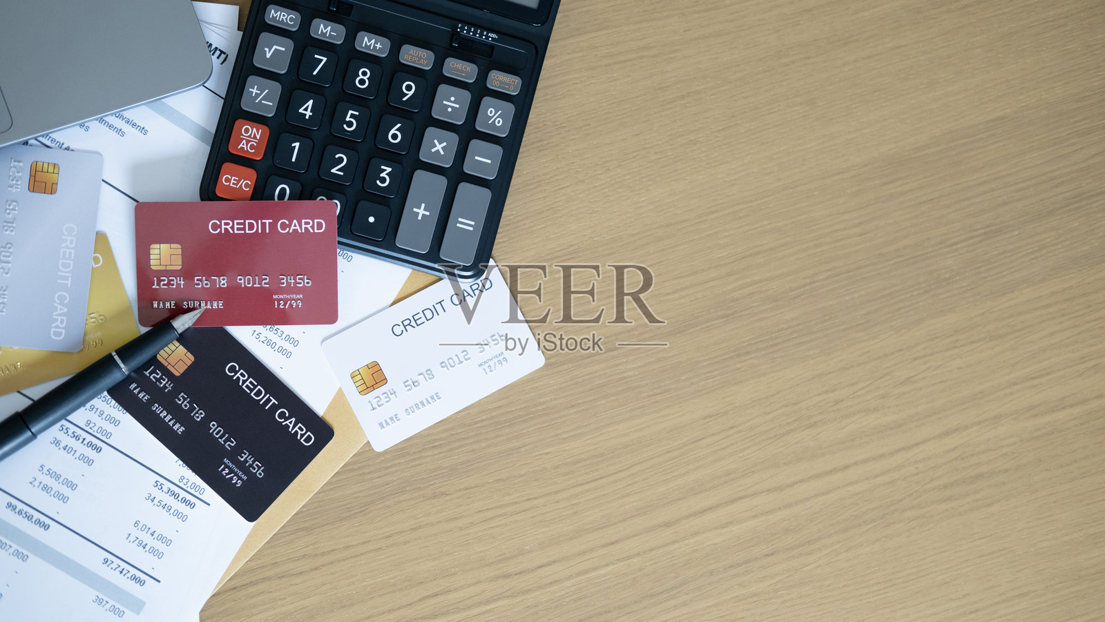 木制办公桌上散落着计算器、笔和彩色信用卡，旁边是财务报表，突出了预算、支出控制和财务规划策略。照片摄影图片