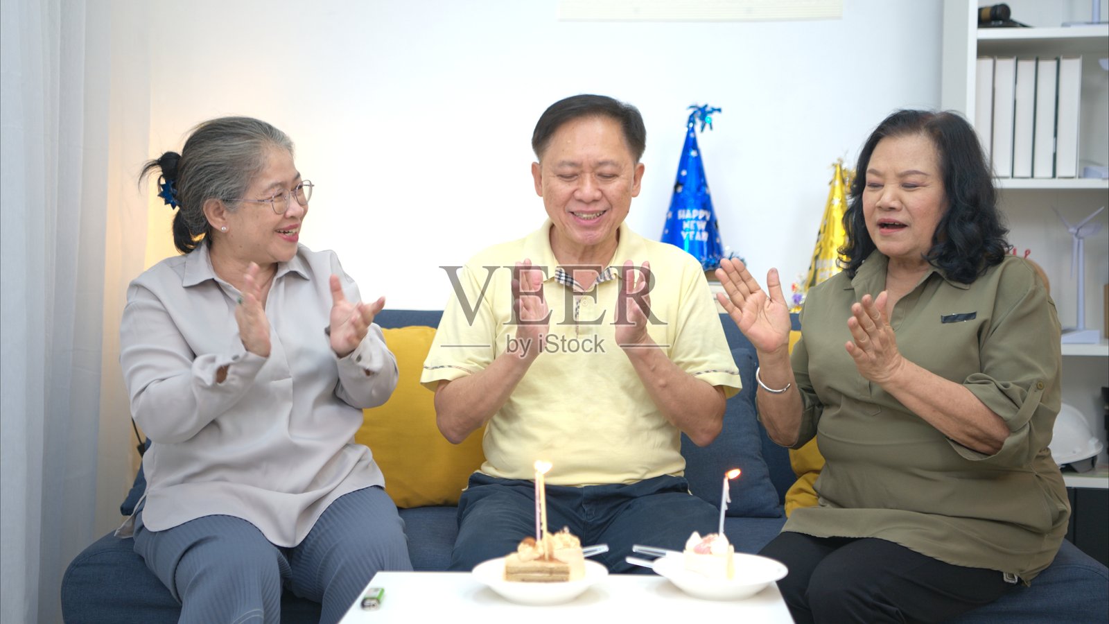 快乐的老年男子在家吹生日蜡烛，朋友们围绕着他，大家一起吃蛋糕、唱歌、跳舞庆祝。照片摄影图片