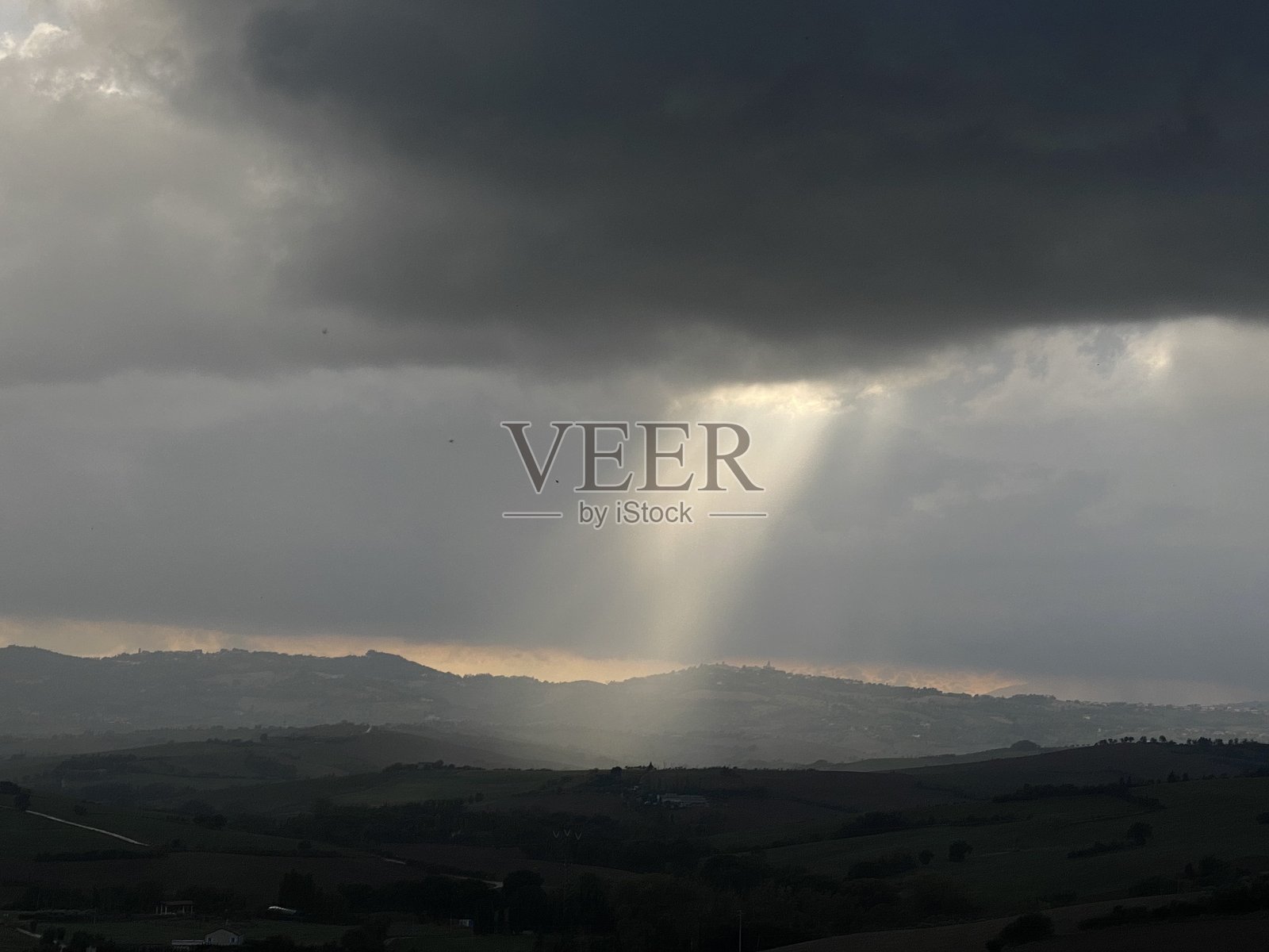 阳光穿透乌云，照亮意大利马尔凯乡村连绵起伏的山丘。照片摄影图片