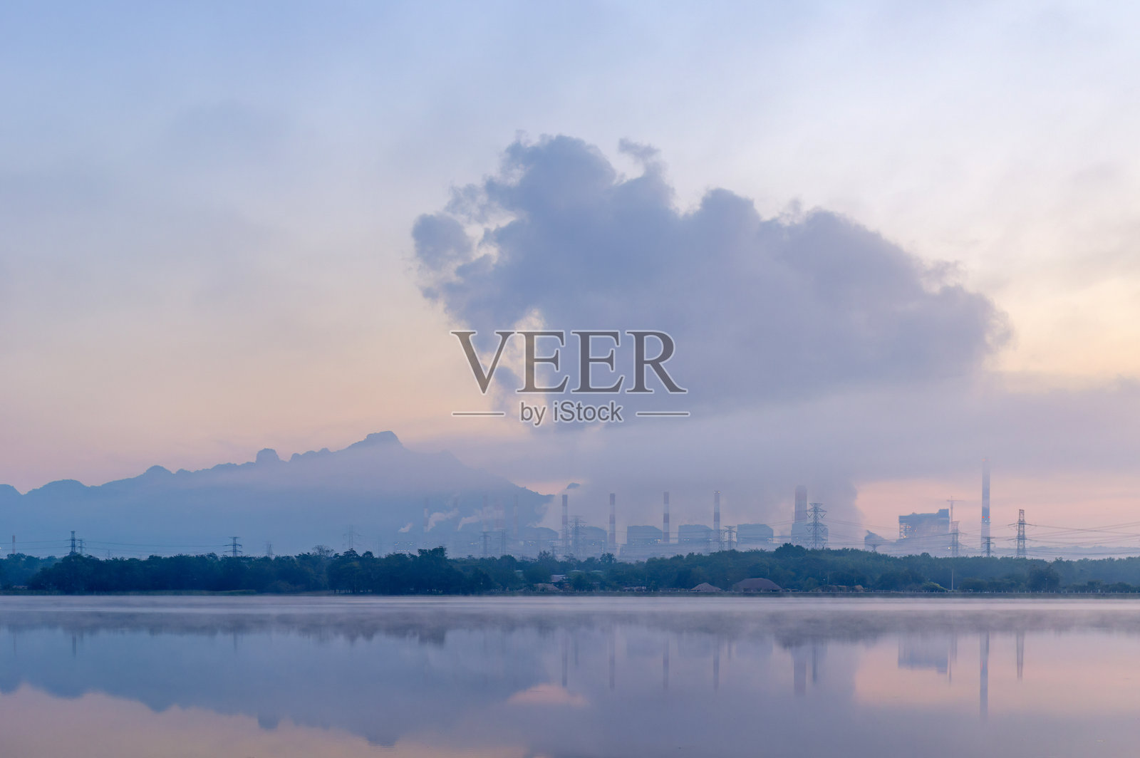 泰国兰邦府，Mae Mo燃煤电厂在黄昏时分的戏剧性景象。煤电站的蒸汽烟雾与薄雾倒映在湖水中，凸显了泰国北部的工业、能源和环境影响。照片摄影图片