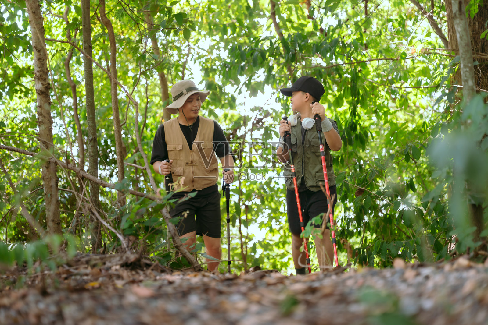 两位徒步旅行者在阳光明媚的自然日里探索一片郁郁葱葱的绿色森林小径，并愉快地谈论着他们的冒险经历。照片摄影图片