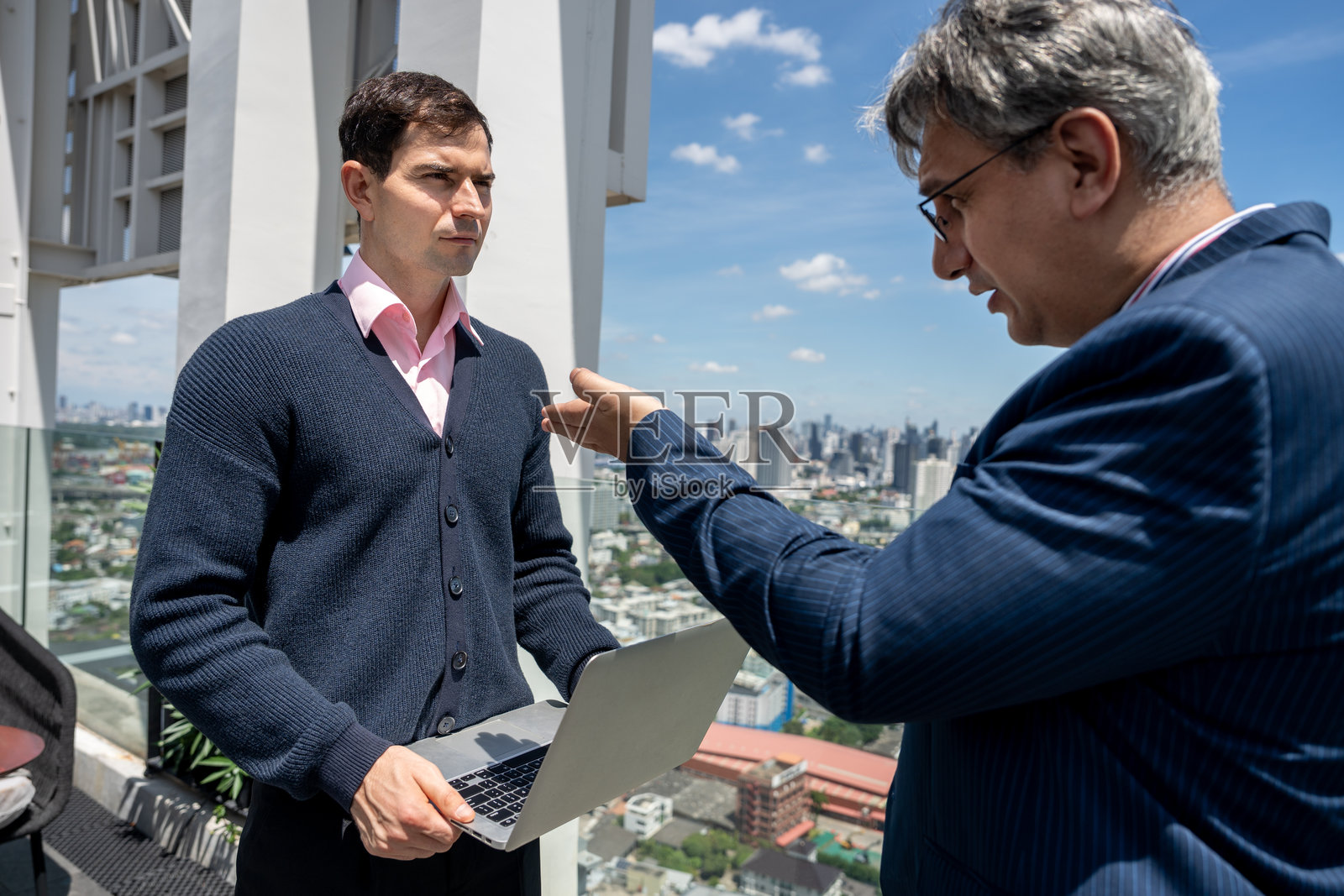 两名商务人士在屋顶办公室进行严肃的讨论，背景为城市景观。照片摄影图片