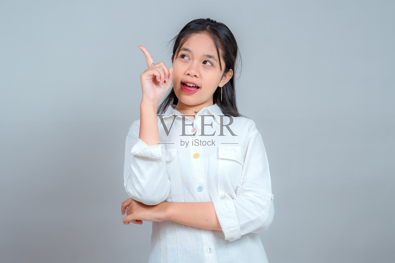 一位身穿白衬衫的年轻亚洲女性肖像，表情好奇而兴奋，伸出食指指向上方，仿佛有了一个绝妙的主意或解决方案。照片摄影图片