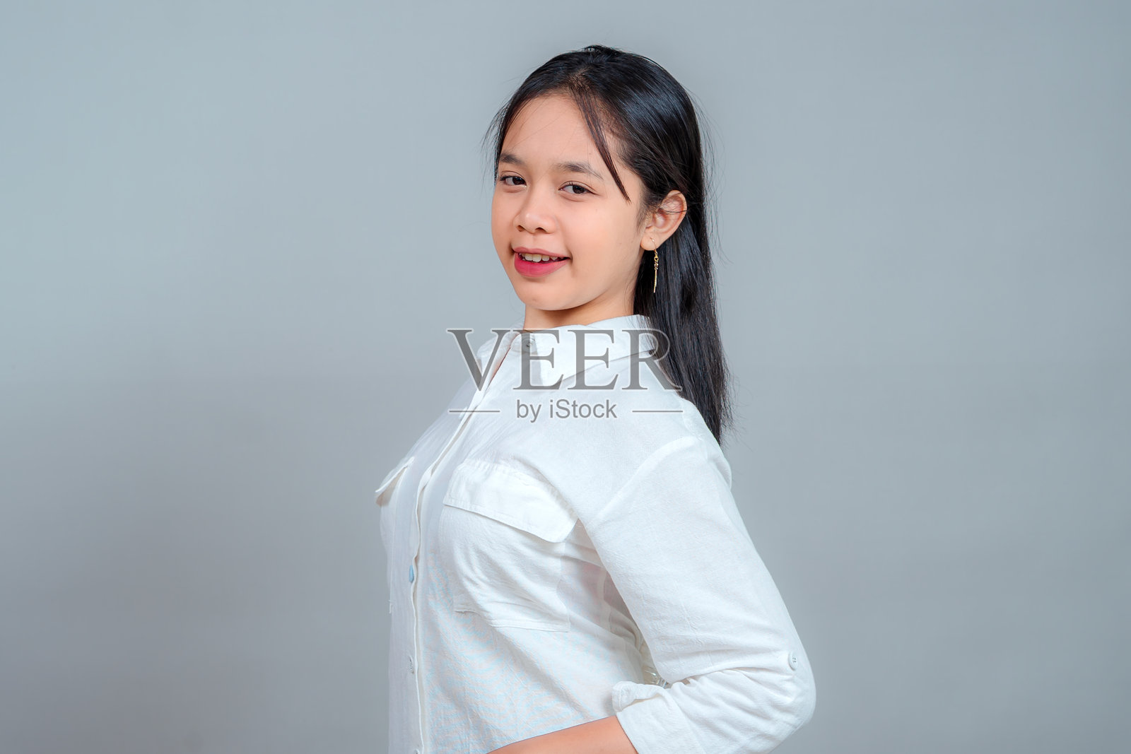 自信的年轻亚洲女性，带着放松的姿势，微微倾斜头部，双手叉腰，脸上带着微妙的微笑。在工作室环境中，表情友好且平易近人。照片摄影图片