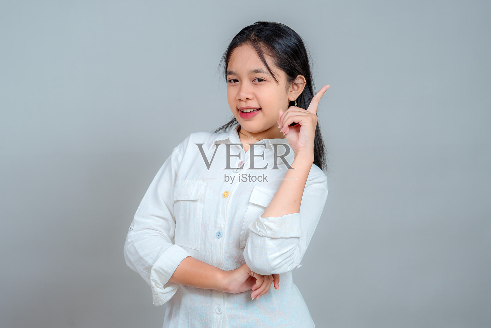 一个穿着白色衬衫的快乐年轻亚洲女孩，竖起食指，带着自信的微笑和俏皮的表情，传达了闪闪发光的想法或顿悟的概念。照片摄影图片