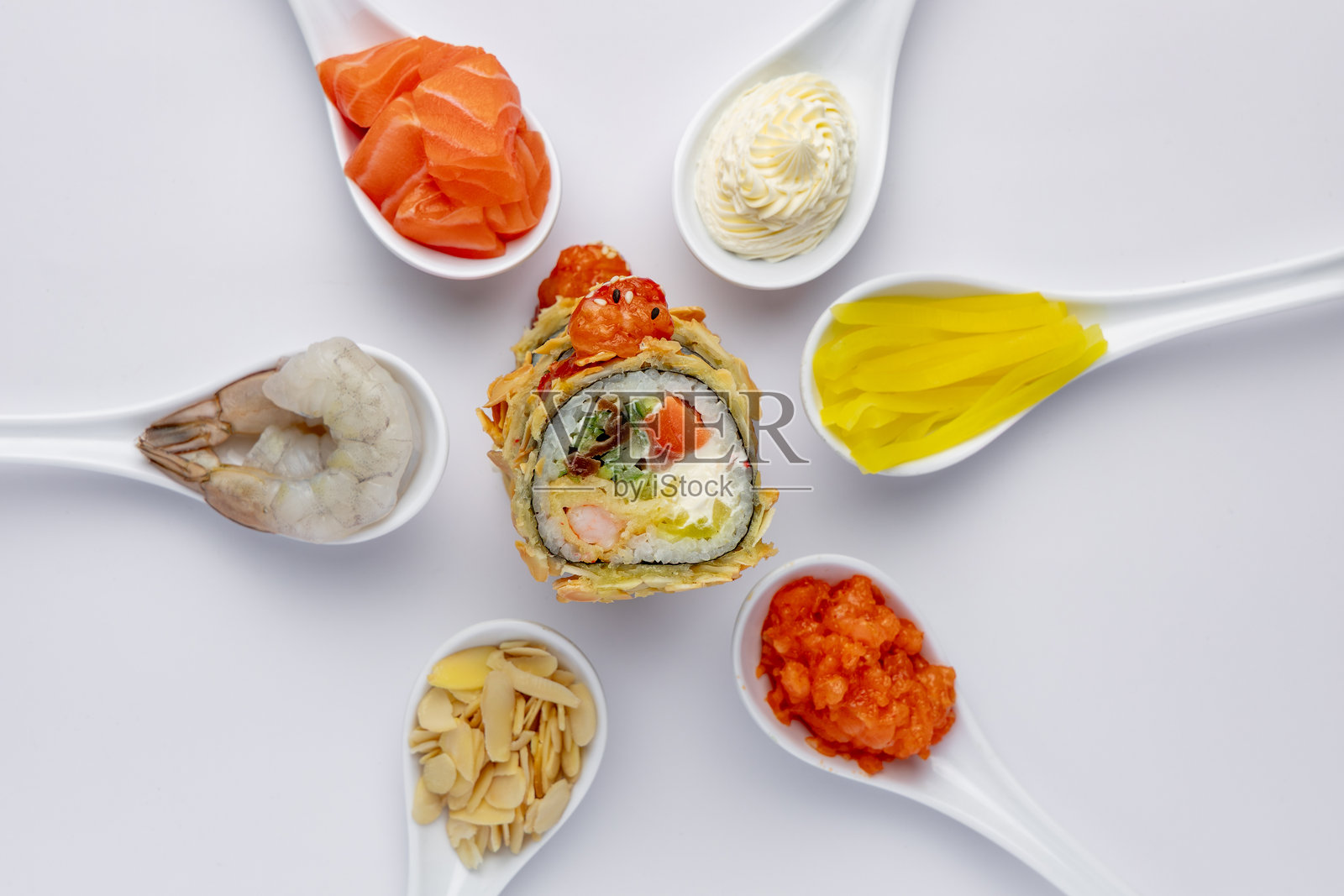 白底寿司卷，周围是带有食材的白色勺子。三文鱼、虾、金枪鱼照片摄影图片