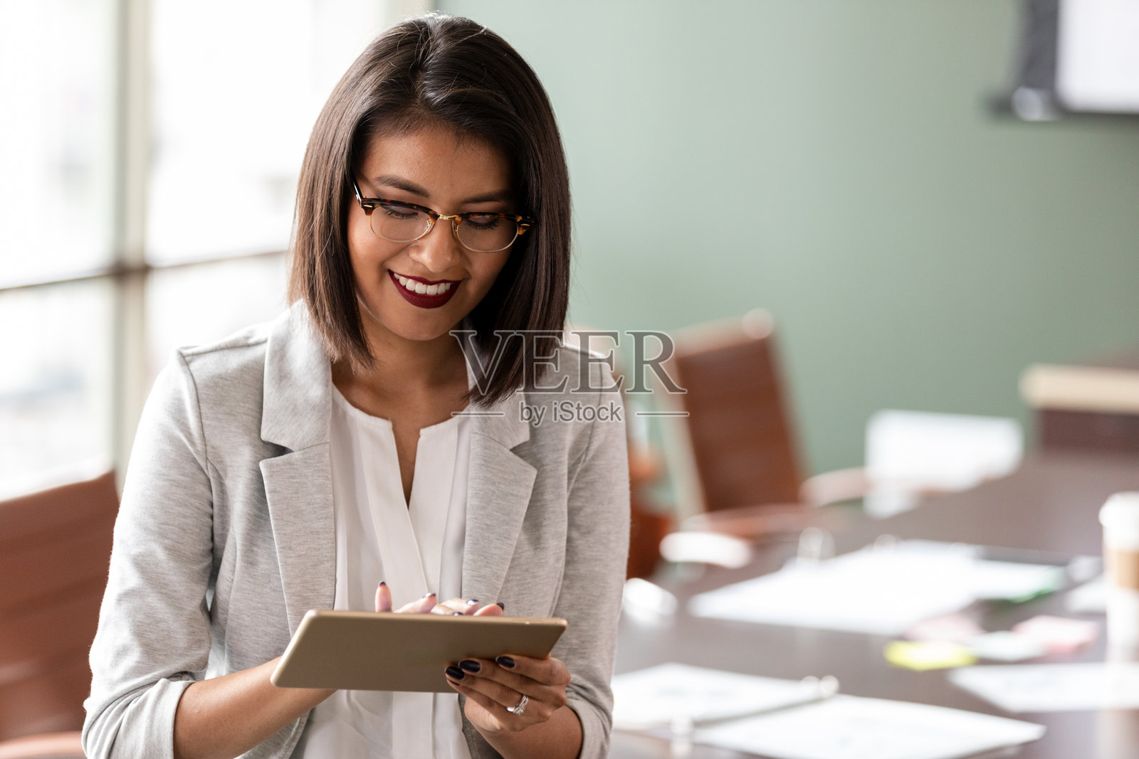 一位职业女性在现代办公室环境中微笑着使用平板电脑工作。照片摄影图片