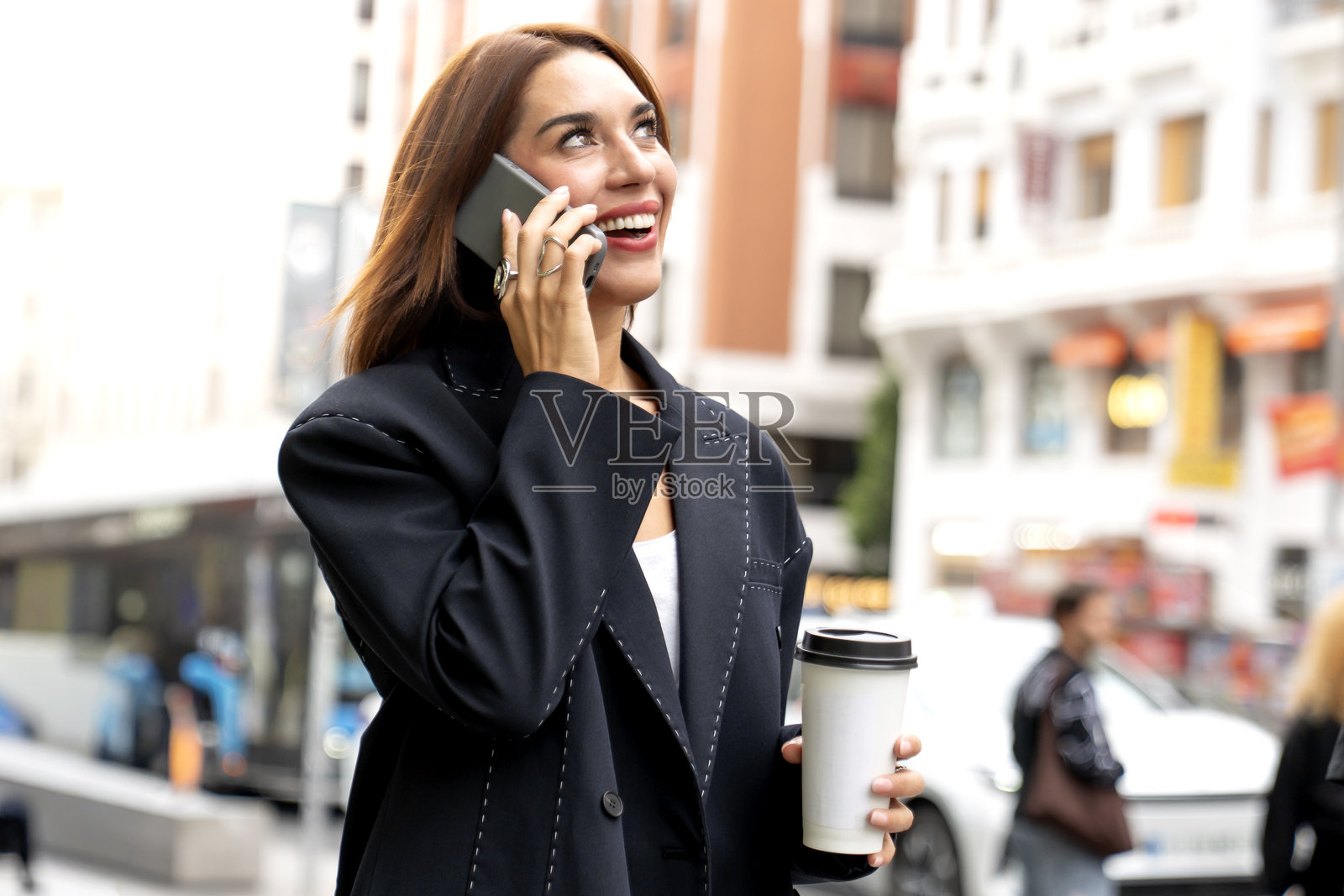 自信的女性在现代城市街道户外，手持咖啡杯和智能手机，面带微笑。照片摄影图片