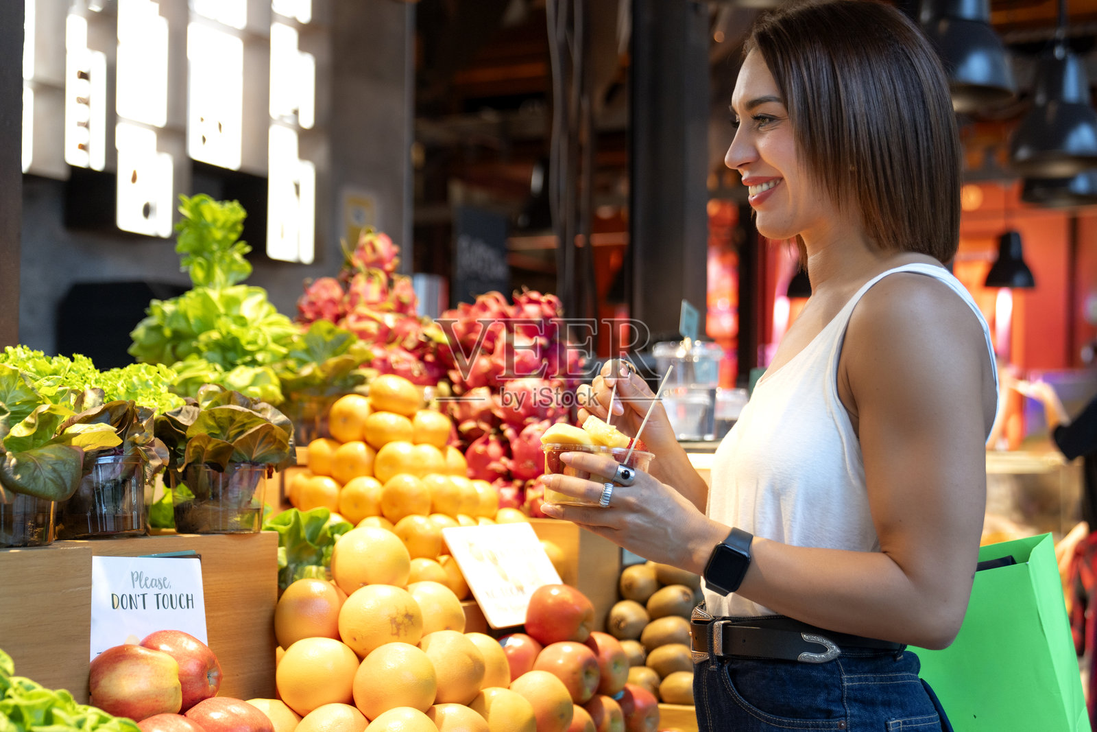 快乐的女人在室内市场购物时，品尝着新鲜的水果杯，面带微笑。照片摄影图片