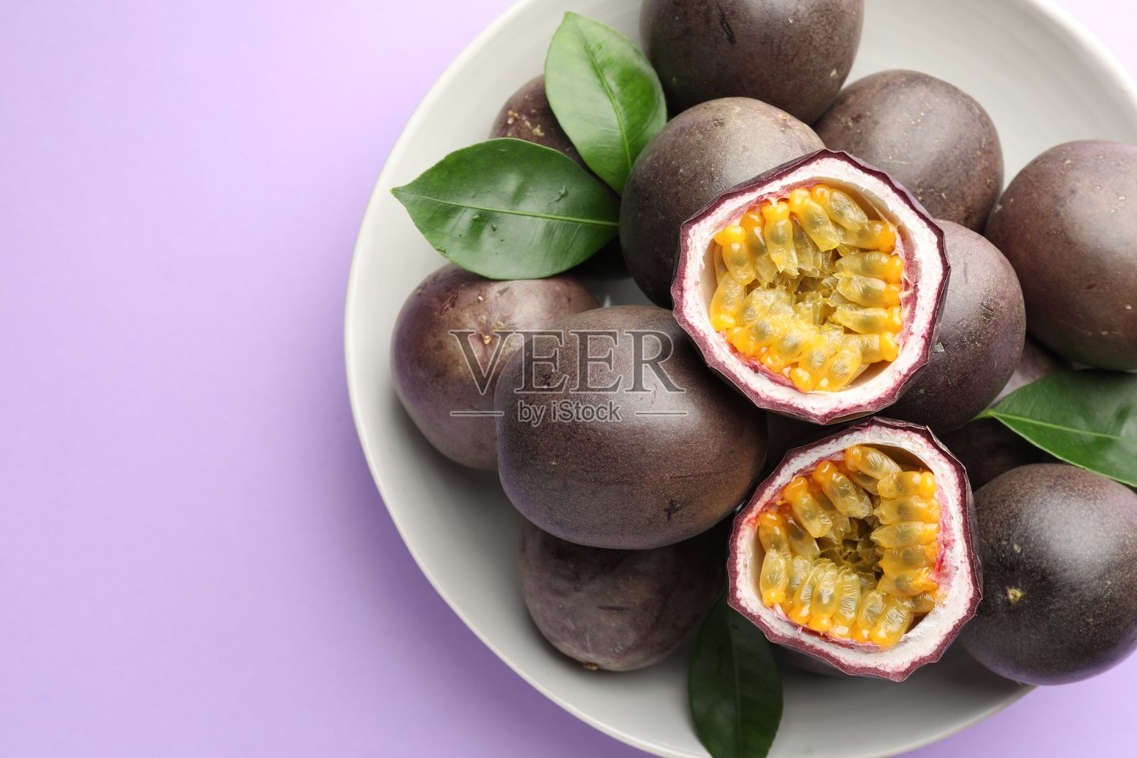 紫底上的新鲜百香果和绿叶，俯视视角照片摄影图片