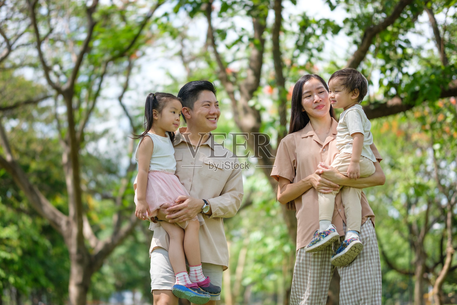 阳光明媚的日子里，一家亚裔人在绿意盎然的公园里愉快地一同散步。照片摄影图片