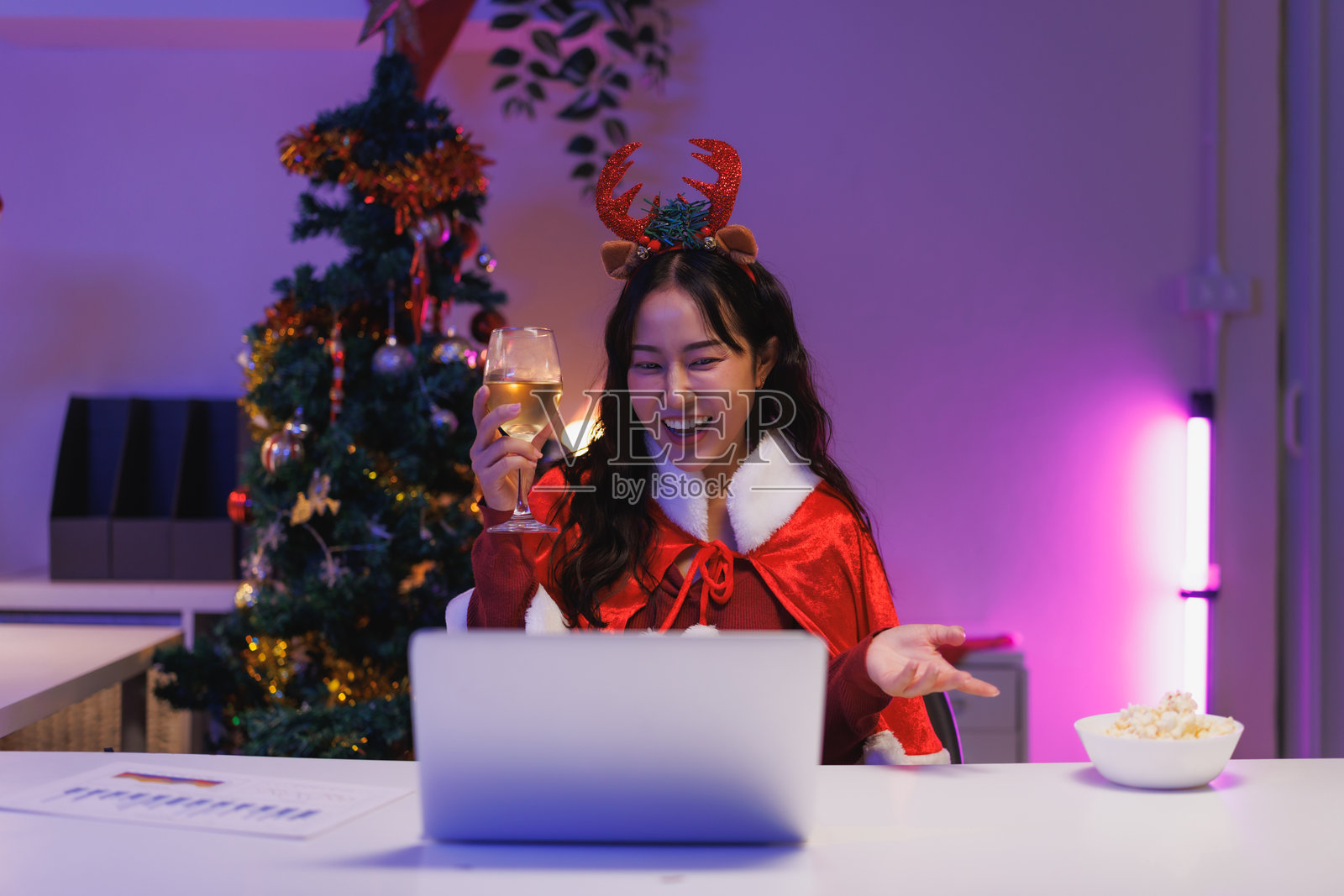 女子在家中通过视频通话庆祝圣诞节，手持一杯葡萄酒。照片摄影图片