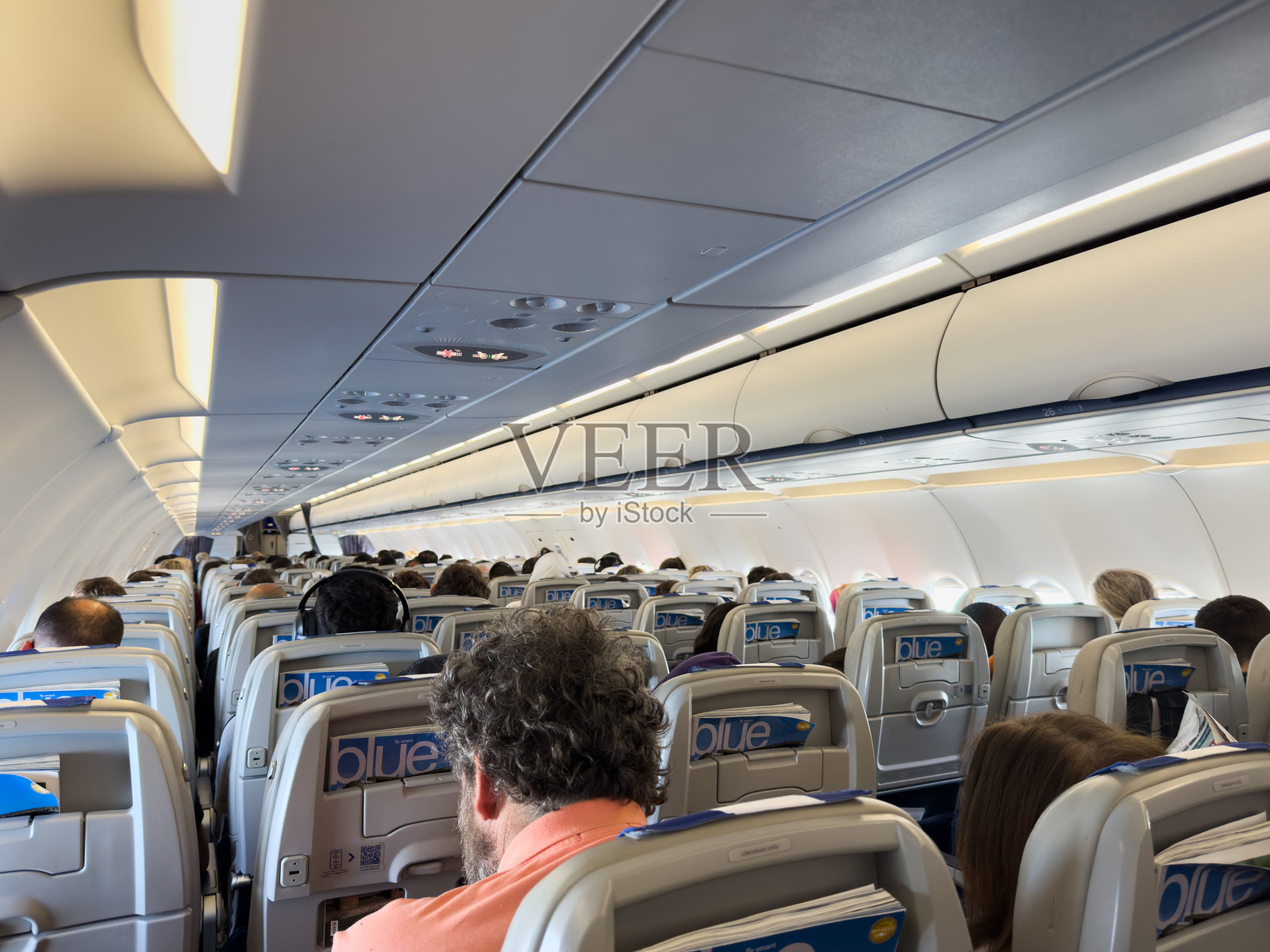 雅典至阿姆斯特丹航班。乘客坐在商业飞机客舱内，可以看到一排排座位和头顶上的行李箱。照片摄影图片