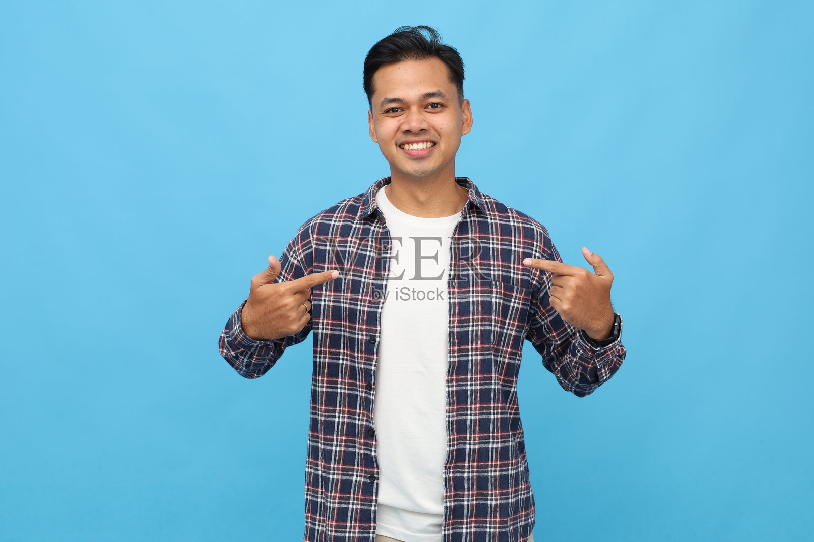 一个穿着休闲服、兴奋又开朗的年轻亚洲男性，伸出食指指向自己，自信且为自己感到骄傲，微笑着看向镜头，独自站立在蓝色背景前。照片摄影图片