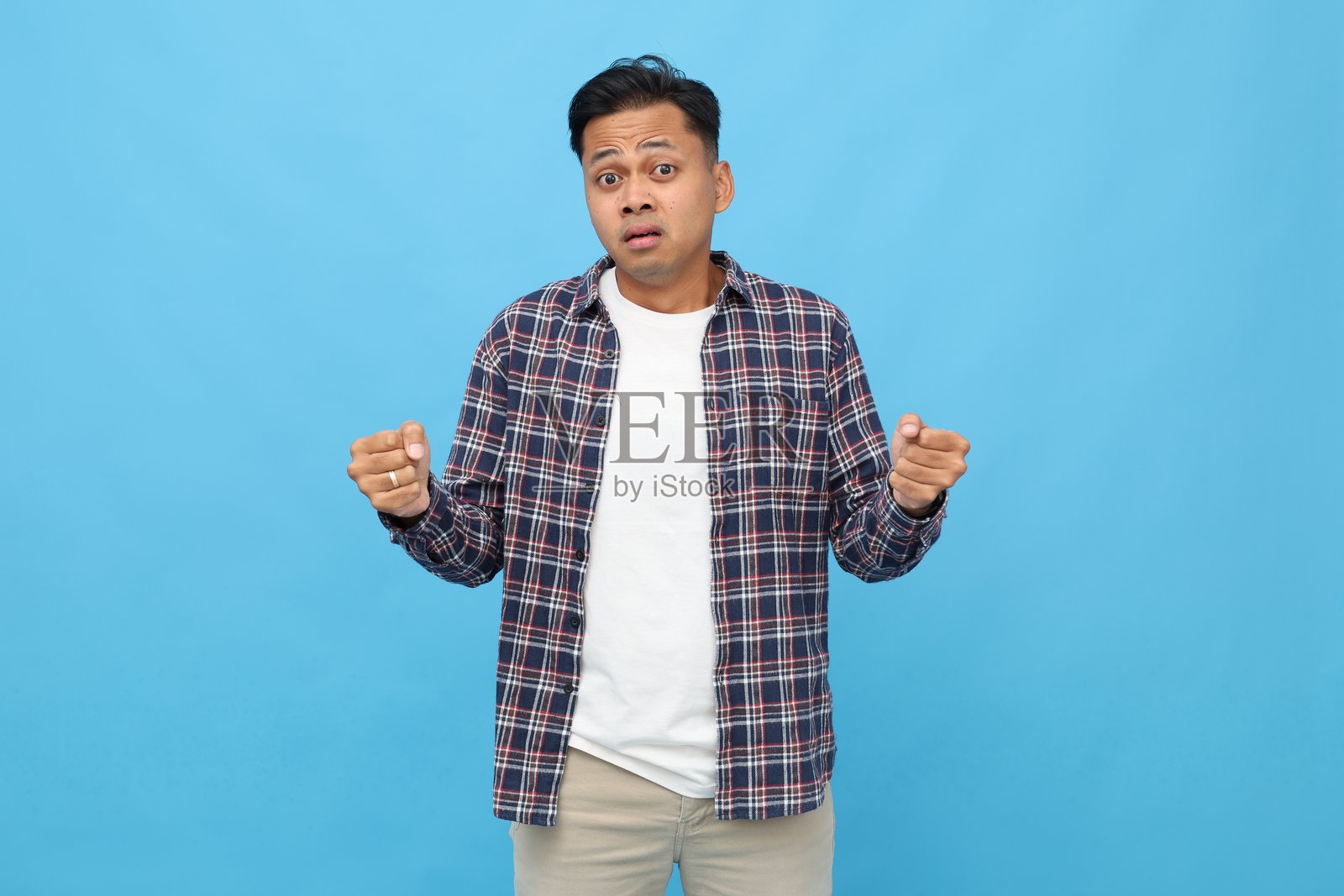 持懷疑態度的年輕亞洲男子展示一個大尺寸物體，皺著眉頭，手裡拿著東西，有供產品推廣廣告的空白空間，孤立在藍色背景上。照片摄影图片