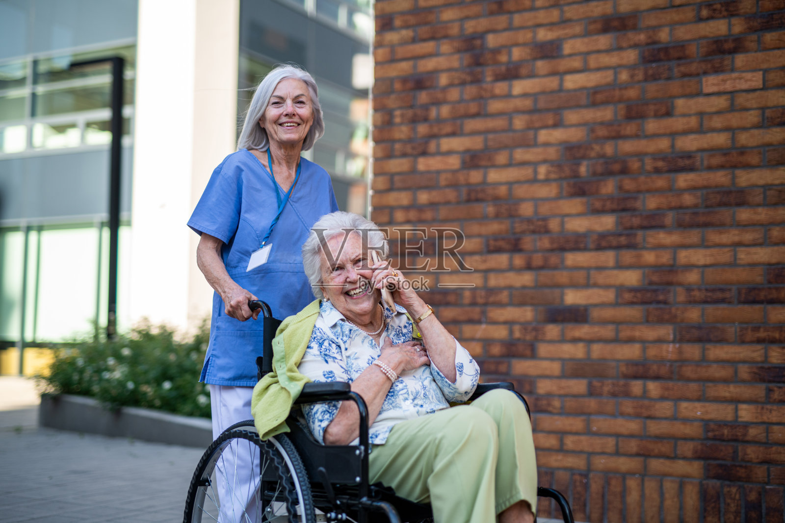 年长的护士在打电话时推着坐轮椅的年长女性。照片摄影图片