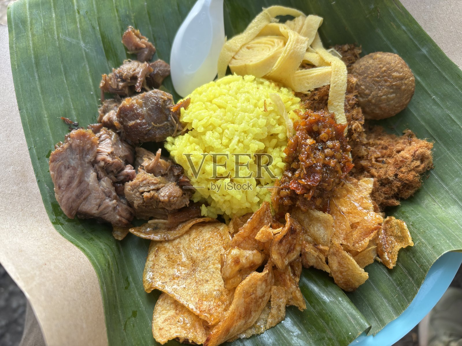 黄姜饭配牛丝、蛋丝、参巴酱和配菜，用香蕉叶盛装，配有塑料勺，适合外带。照片摄影图片
