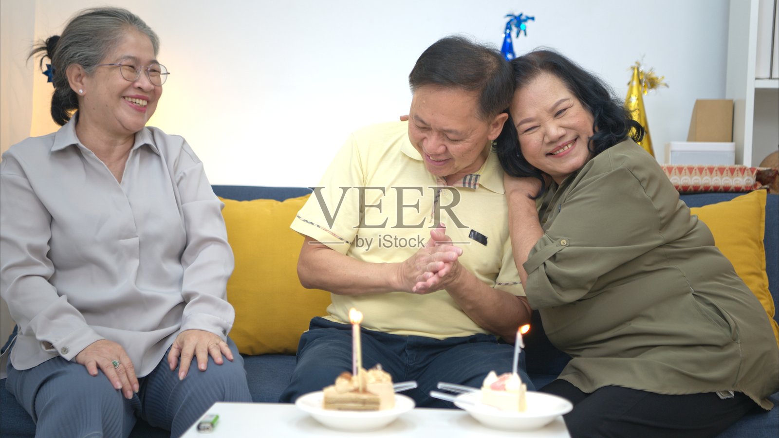 快乐的老年男子在家吹生日蜡烛，朋友们围绕着他，大家一起吃蛋糕、唱歌、跳舞庆祝。照片摄影图片