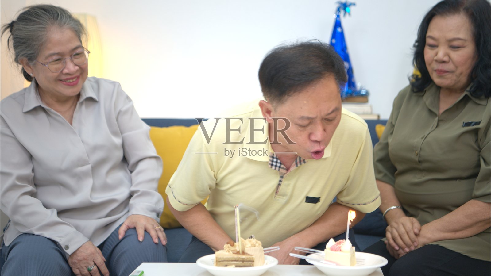 快乐的老年男子在家吹生日蜡烛，与朋友们一起吃蛋糕、唱歌跳舞庆祝。照片摄影图片