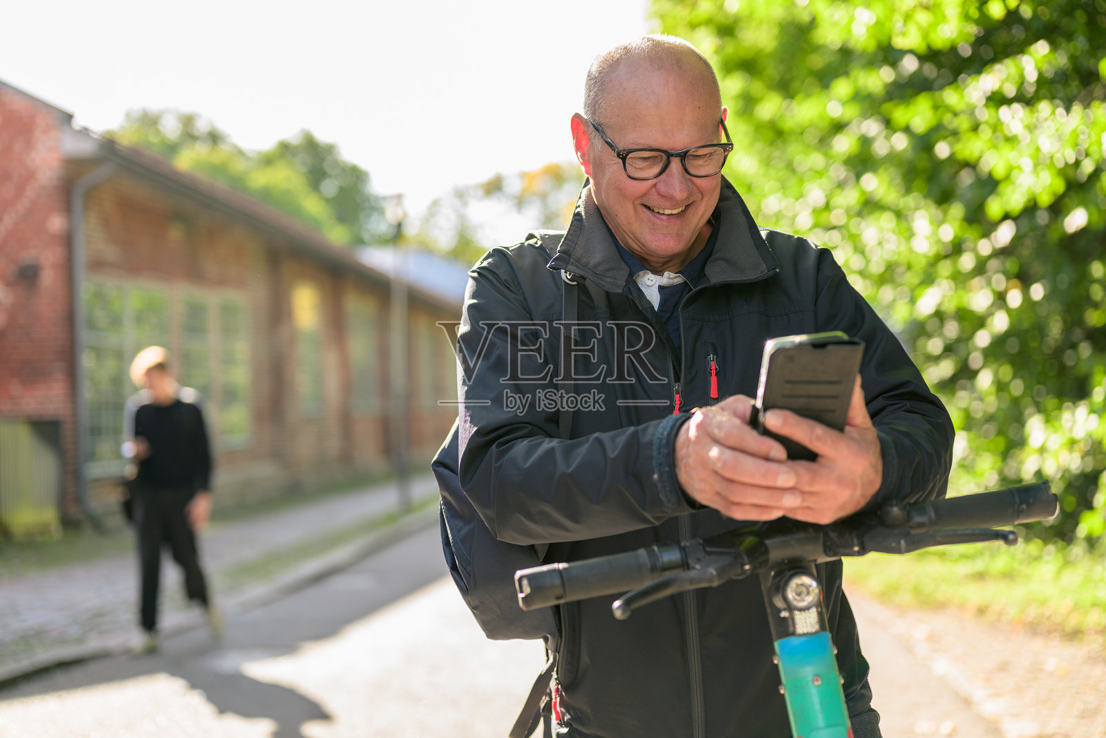 一位年长的男性，面带微笑，在城市中骑着电动滑板车并使用手机。照片摄影图片