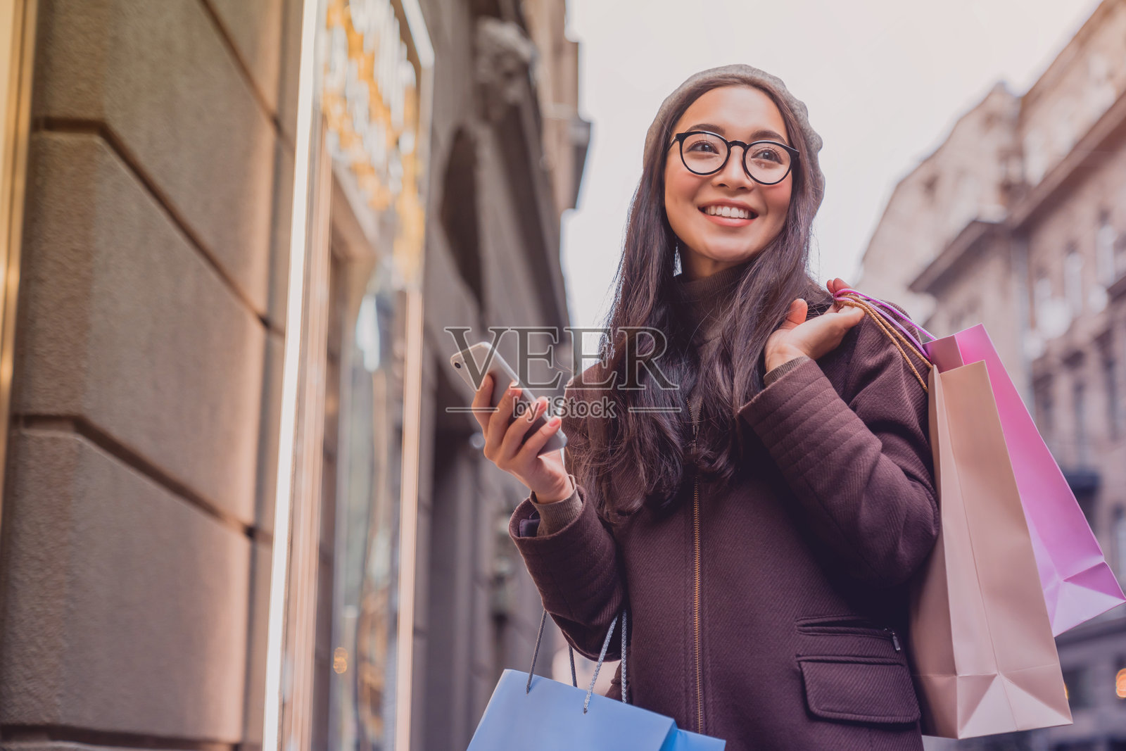 一位亚洲女性在购物日享受时光，同时使用智能手机并看向别处。照片摄影图片