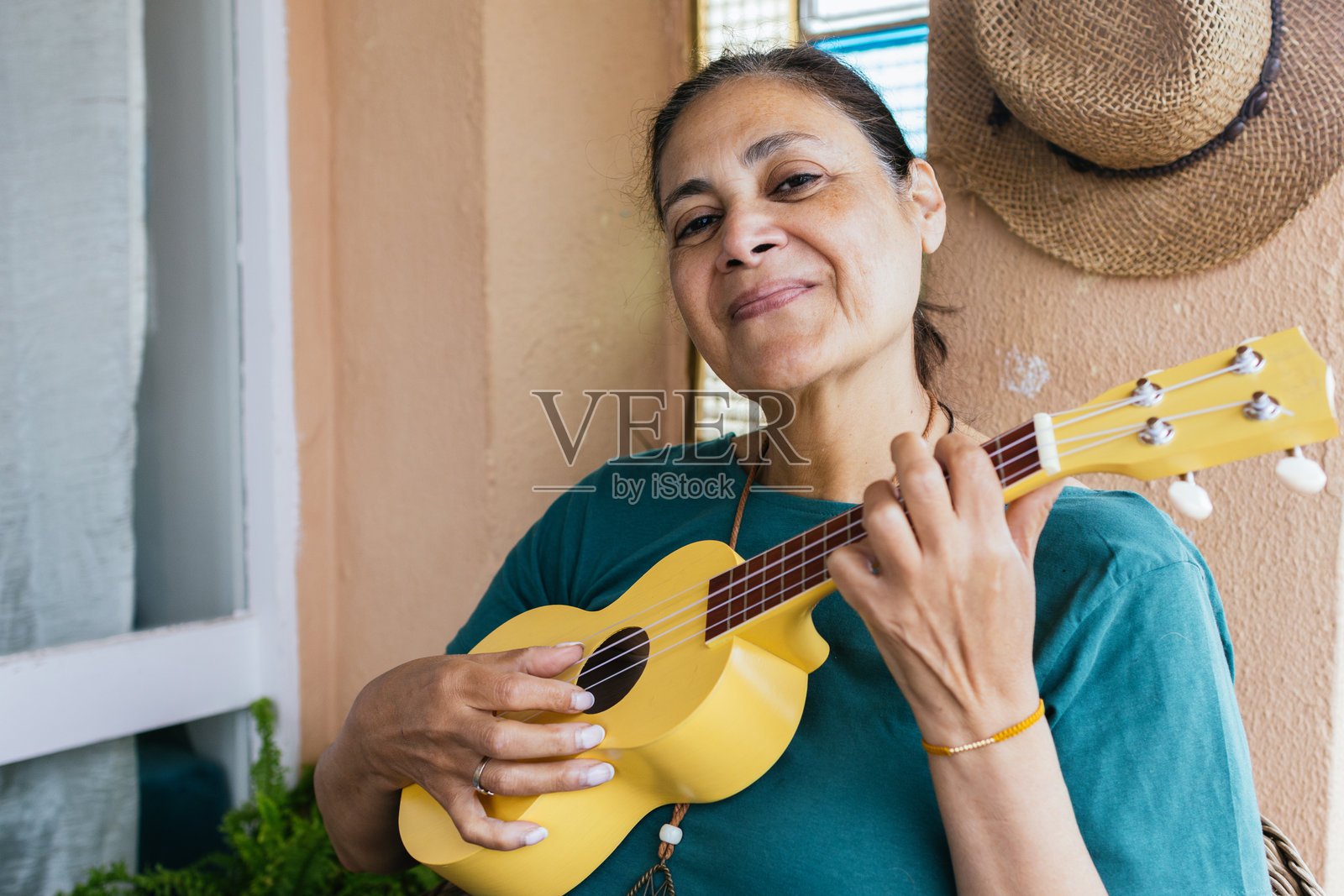 中东民族的成熟的女性微笑着看向镜头，正在用尤克里里演奏音乐。照片摄影图片