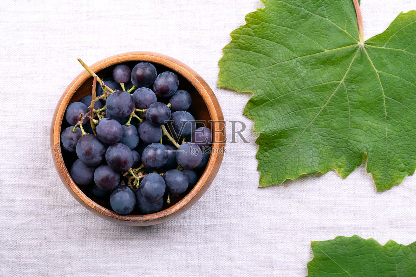 木碗里盛放着葡萄藤的蓝色葡萄，放在亚麻布上。照片摄影图片