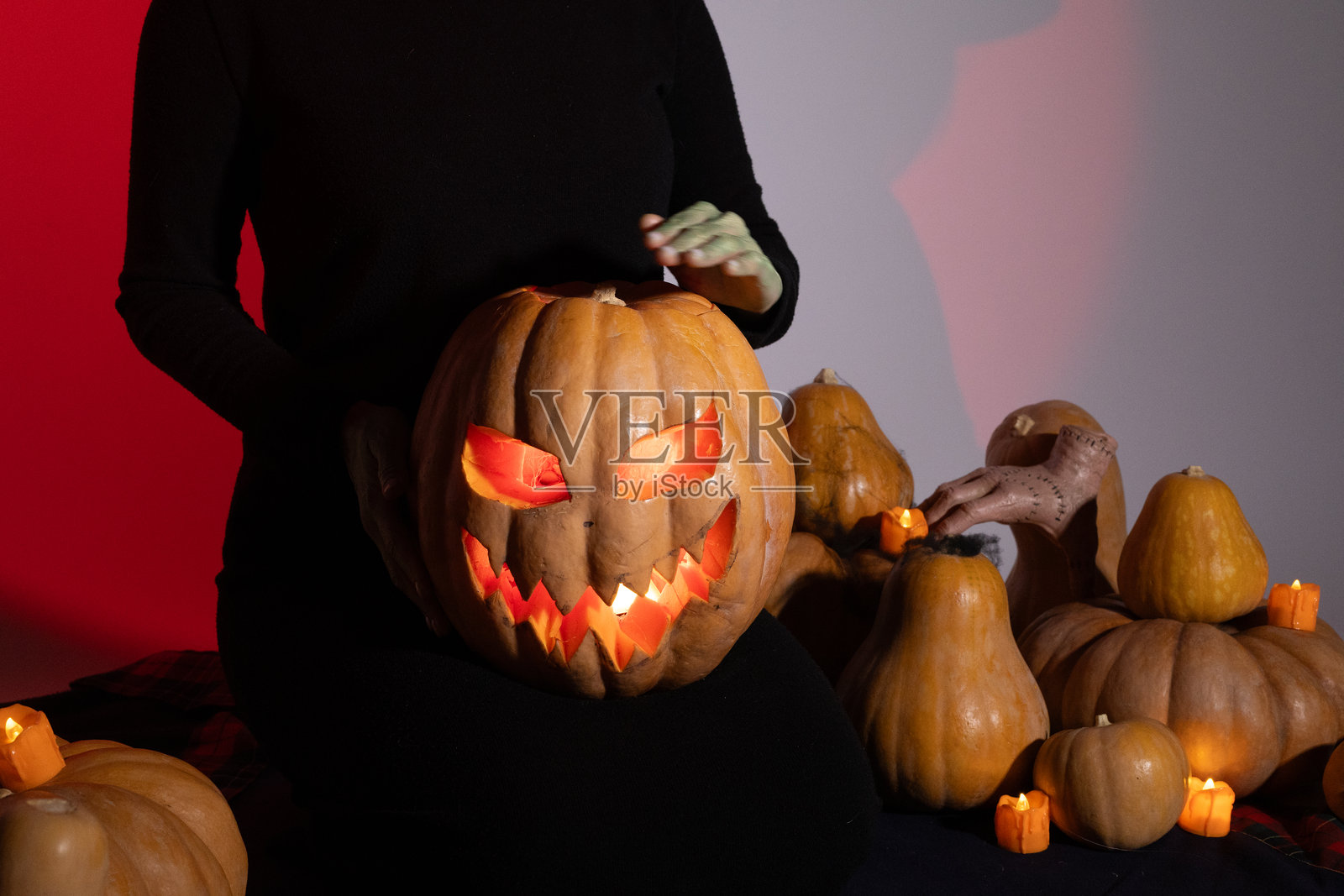 身着黑裙的女子手持雕刻好的南瓜，烛光从后方映照，营造出温暖的光晕。照片摄影图片