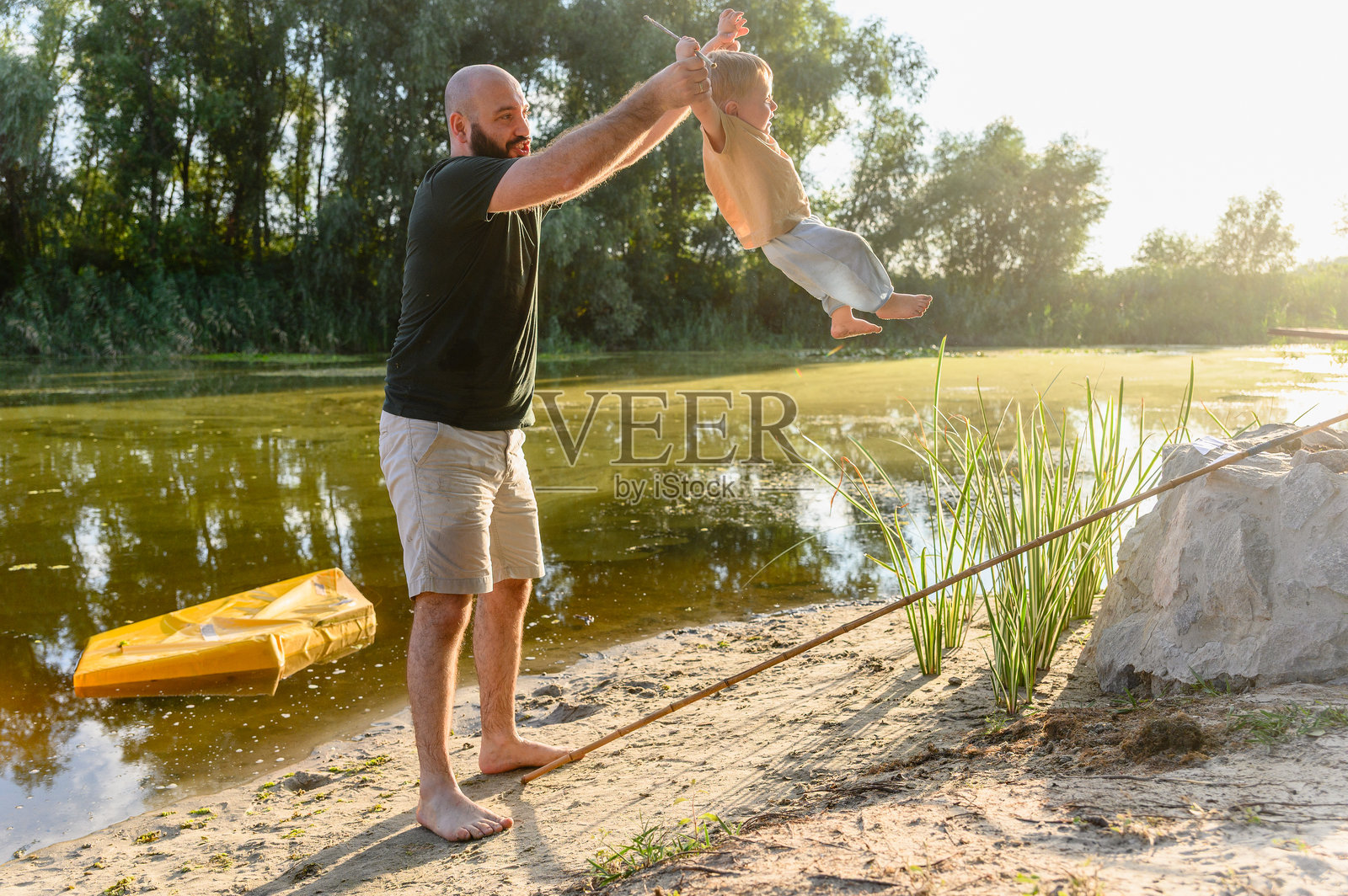 父亲在河边将蹒跚学步的孩子高高举起。照片摄影图片
