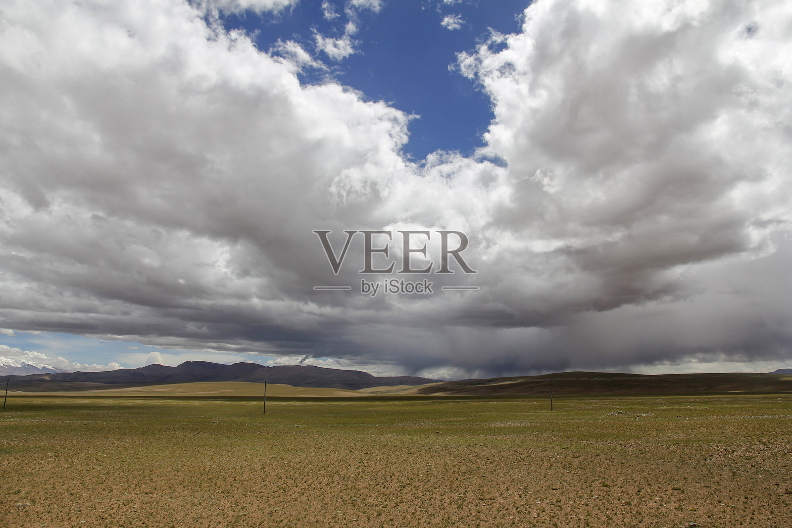 广阔的平原，头顶是戏剧性的多云天空，远处是连绵的山脉照片摄影图片