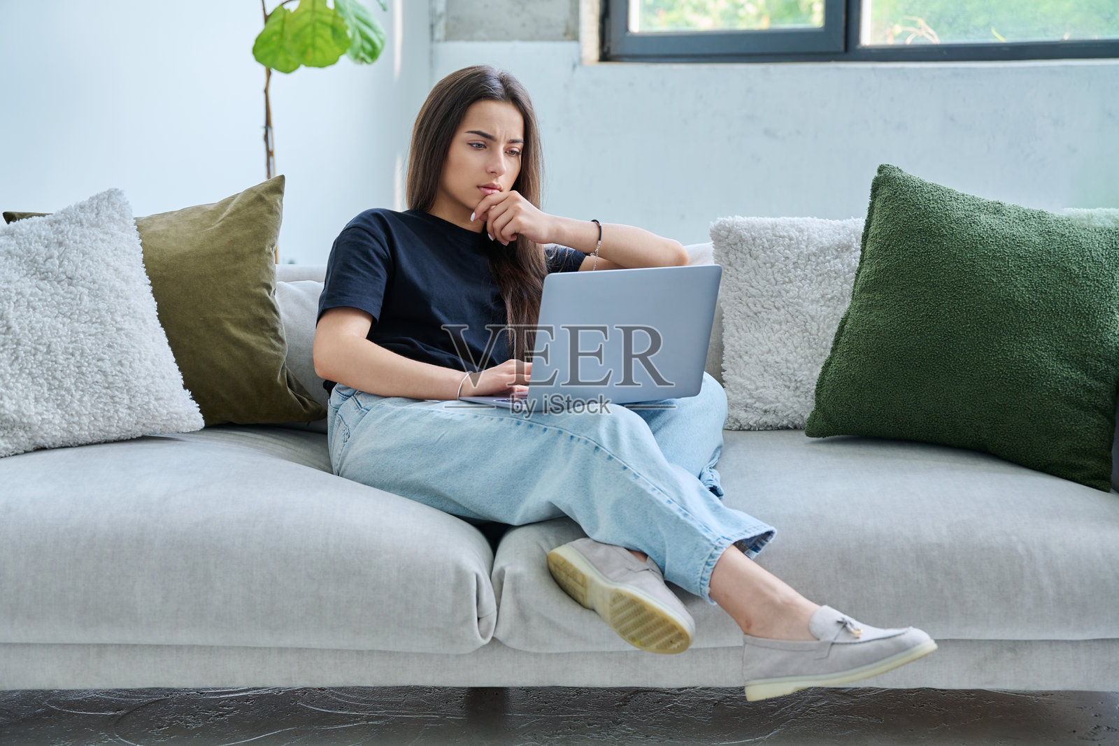 认真的少女坐在家里的沙发上看着笔记本电脑照片摄影图片