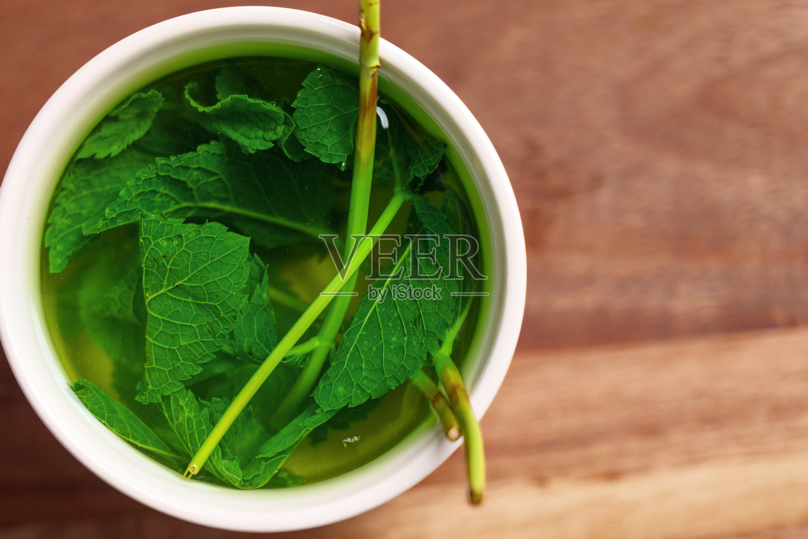 木桌上的马克杯里放着新鲜薄荷和热水。照片摄影图片