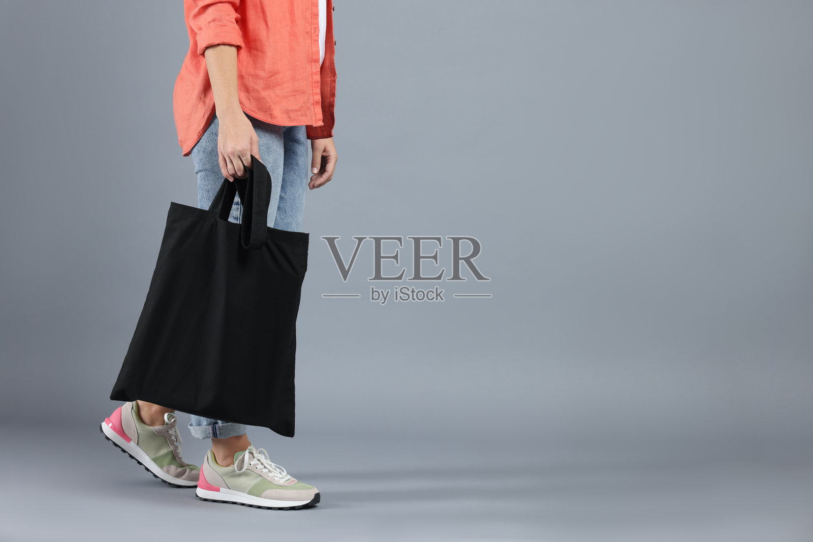 灰色背景下，女子手持空白黑色购物袋，特写。用于设计的模型图照片摄影图片